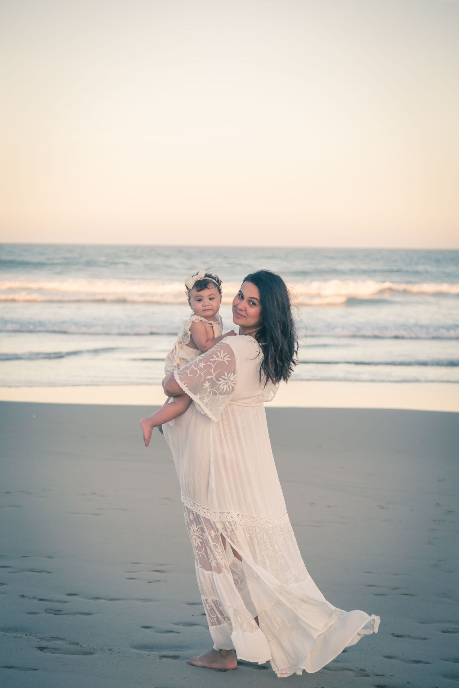 A flowing white lace dress catches the ocean breeze on a serene beach at sunset.