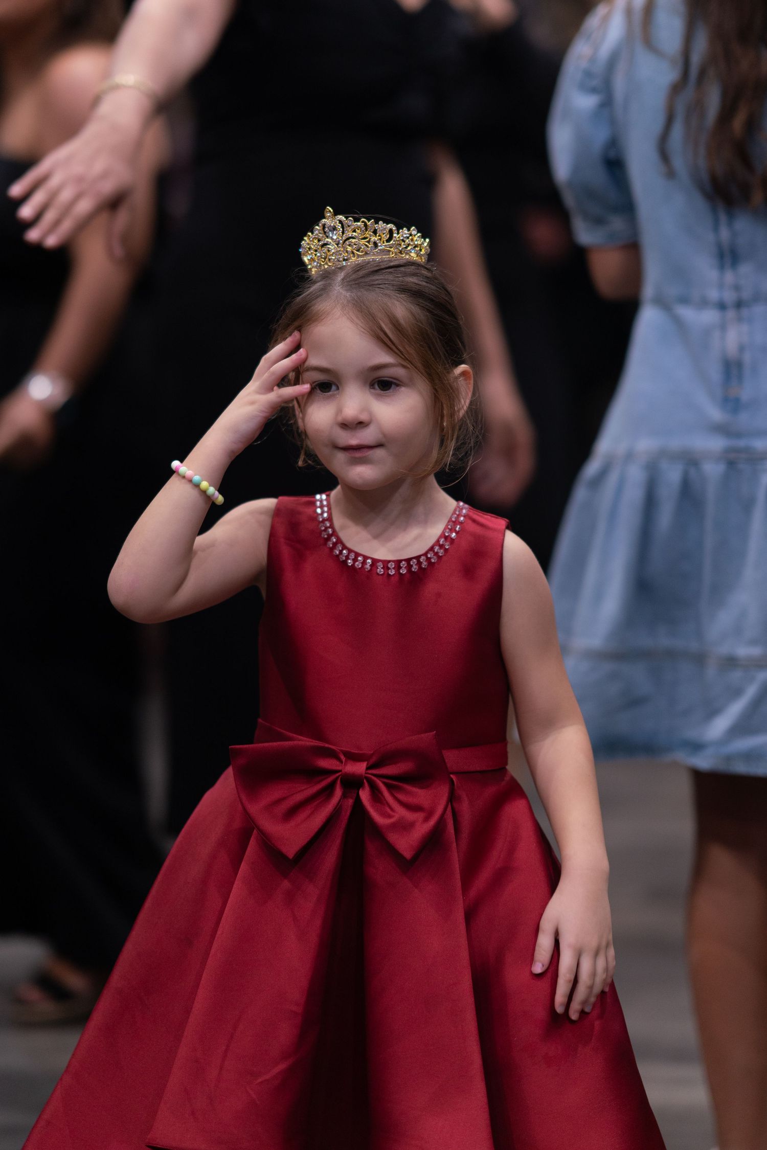 Young attendee in red formal dress with bow and tiara dancing at an event.