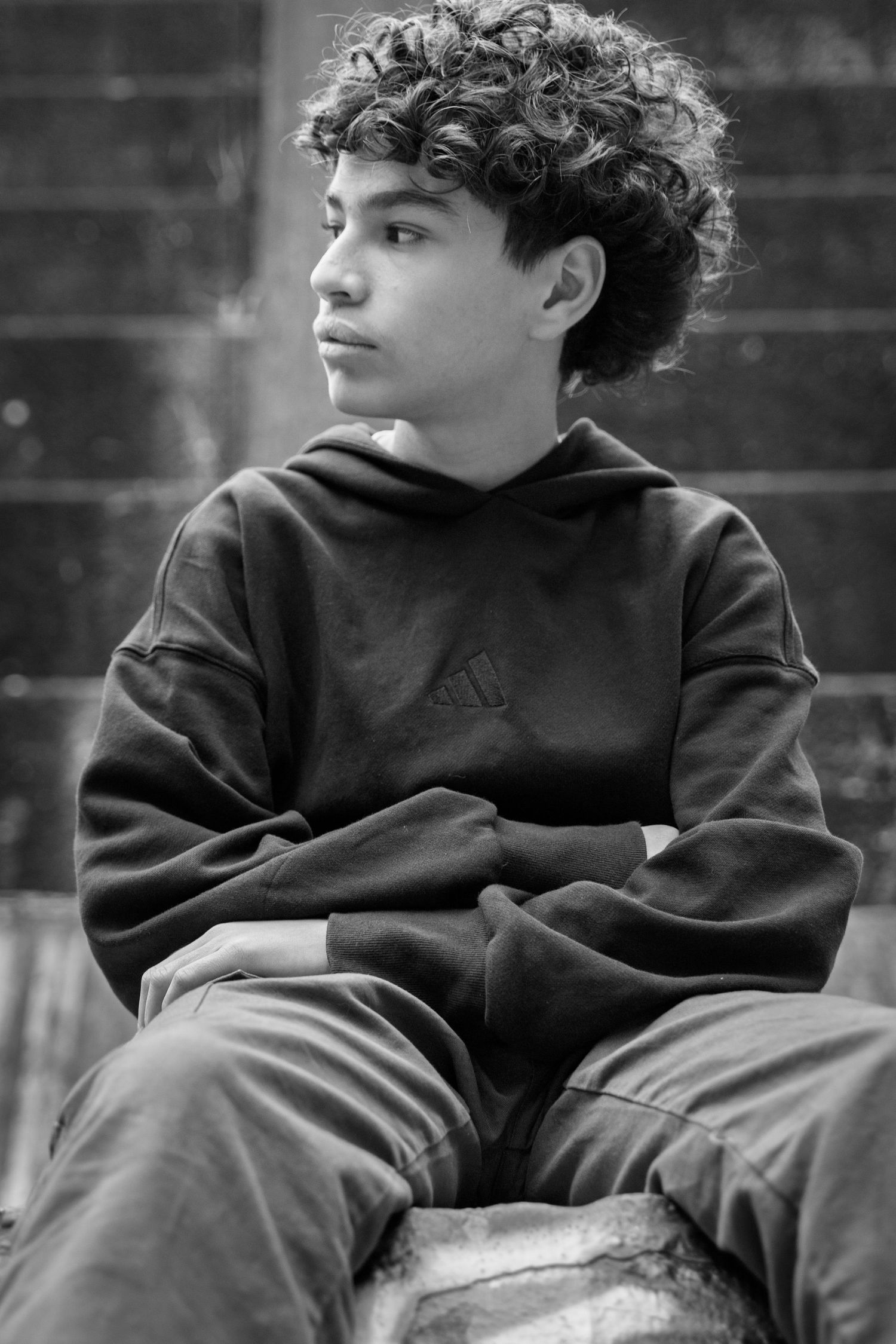 Black and white portrait of person in hoodie with curly hair sitting thoughtfully.