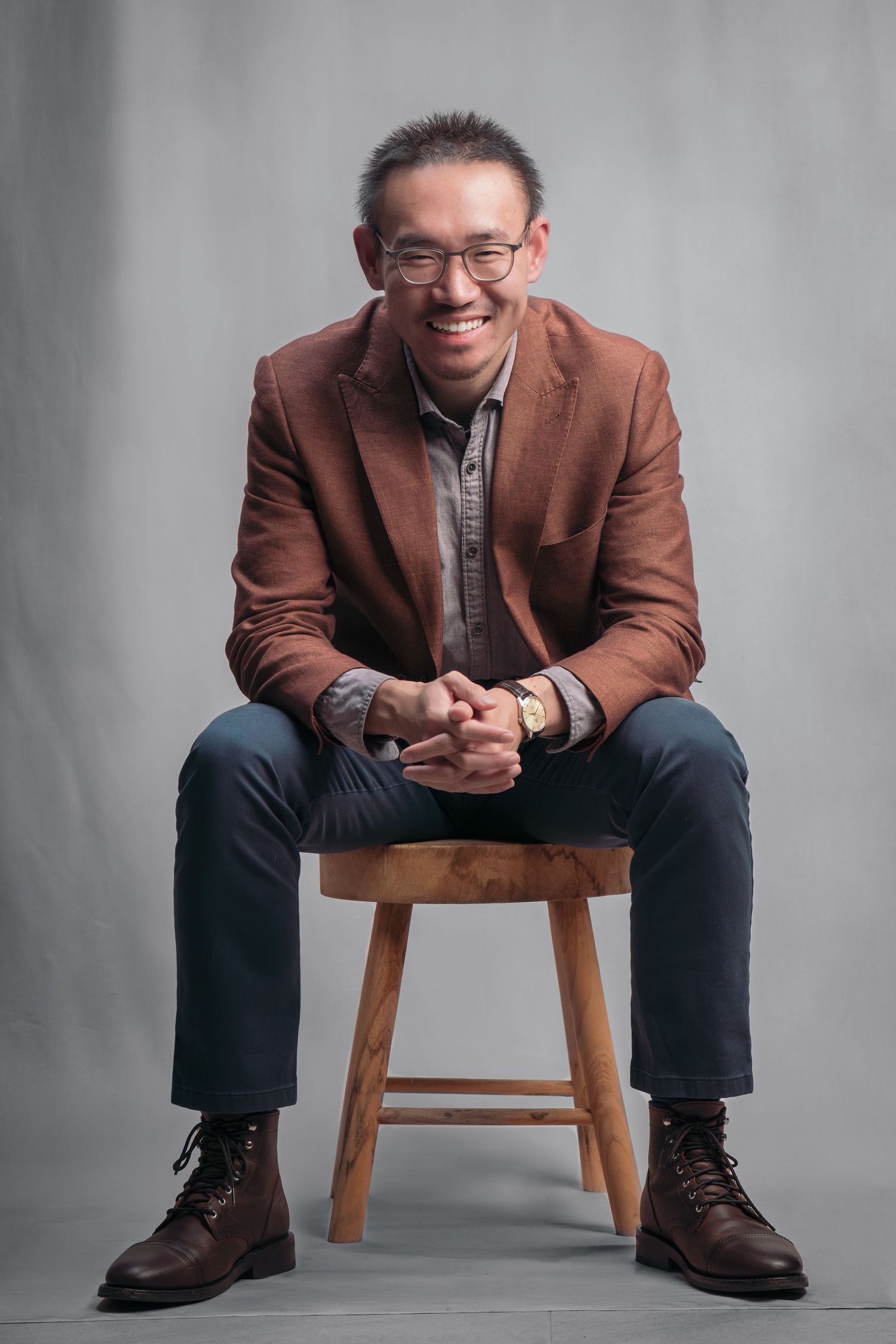 Professional portrait series showing seated figure in brown blazer and dark pants against gray background.