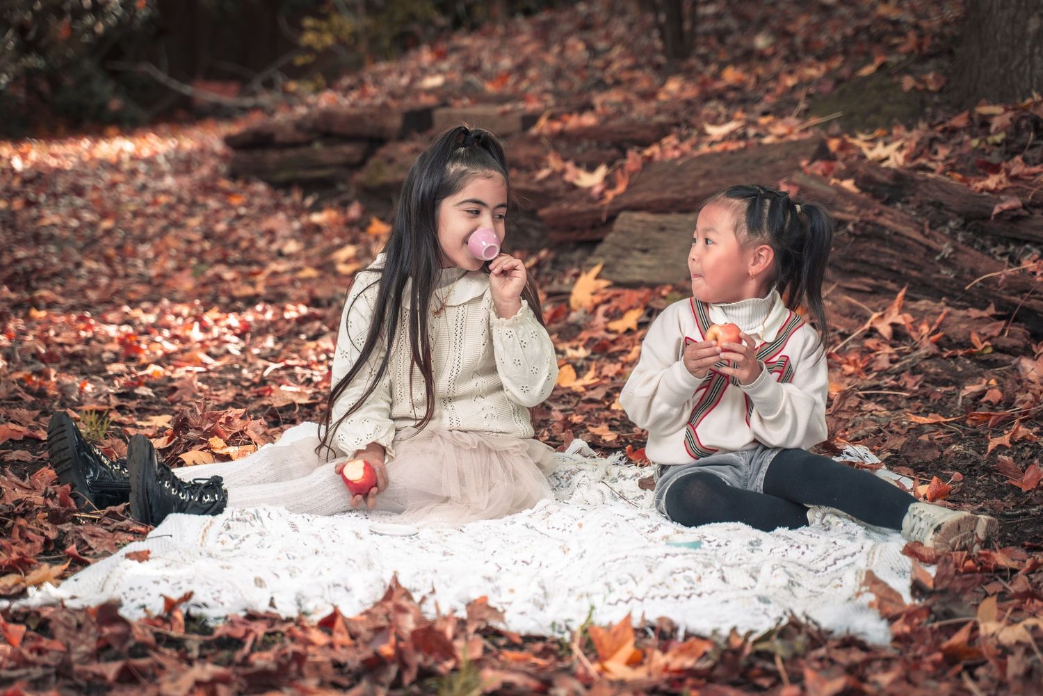 Couple in elegant white attire lies on autumn leaves during outdoor photo session.