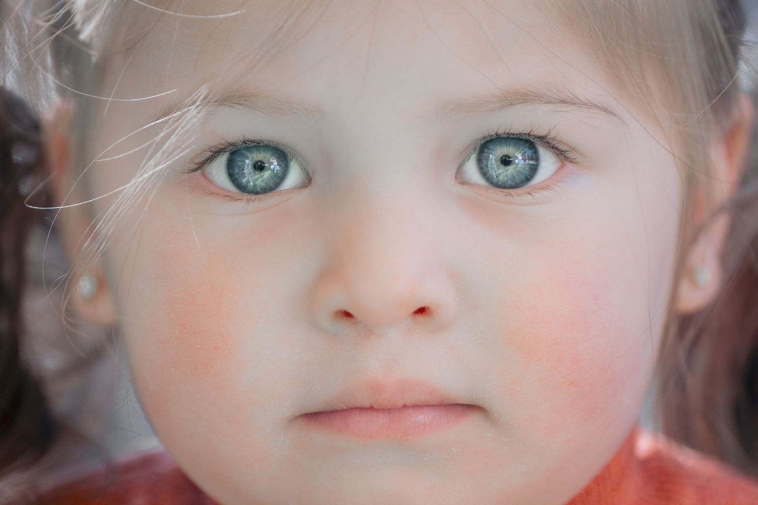 Seven side-by-side portrait style images showing expressive blue eyes and rosy cheeks in soft, warm lighting.