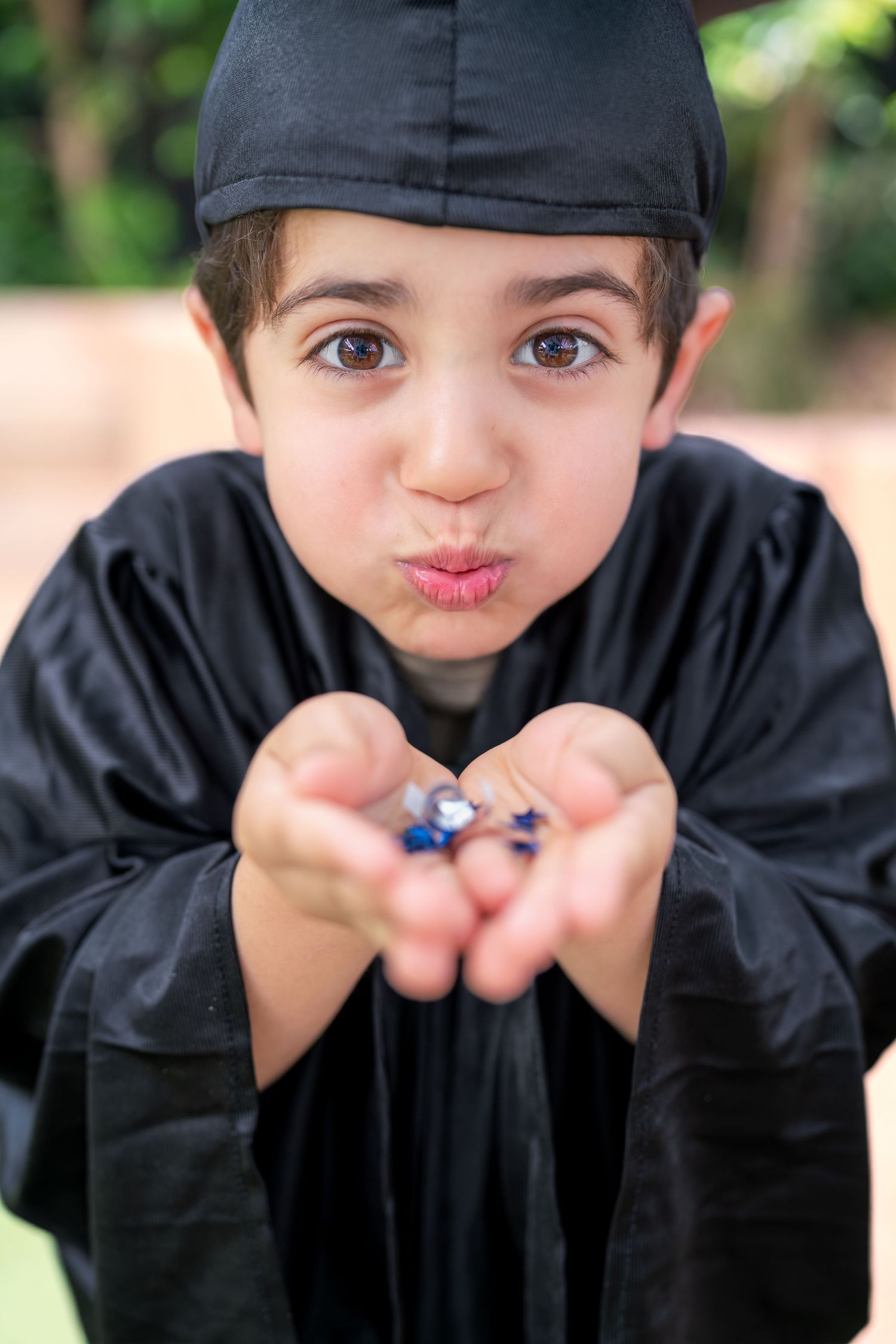 A child in a black graduation gown poses playfully in a series of four connected photos outdoors.
