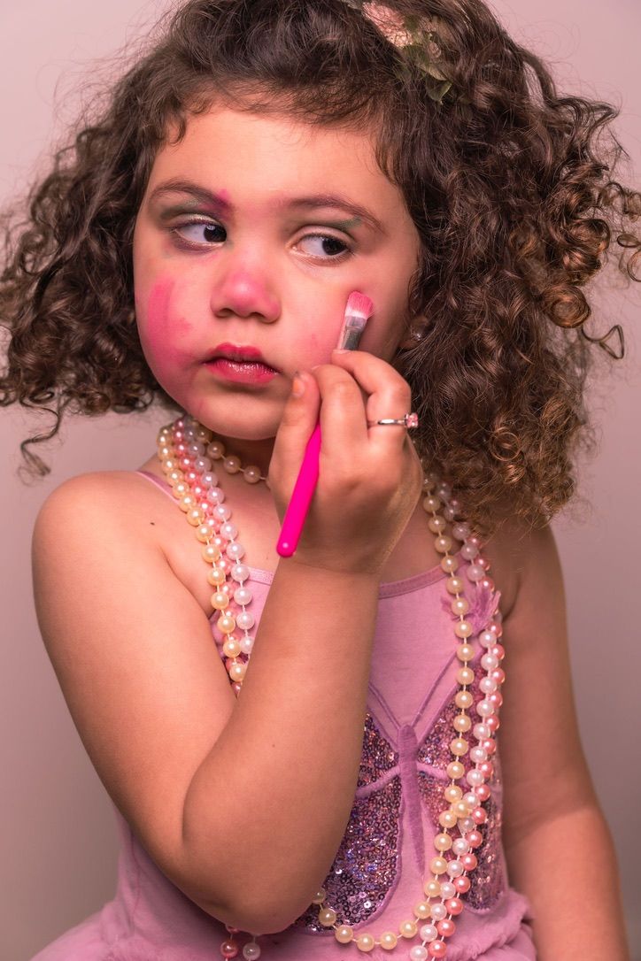 A dramatic portrait featuring curly hair, pearls and pink makeup against a neutral background.