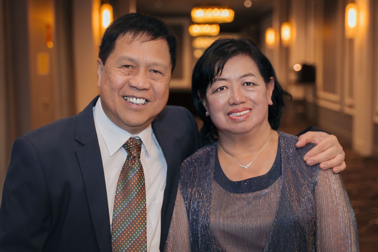 A group of people in formal attire gather at an elegant venue with warm lighting and ornate decor.