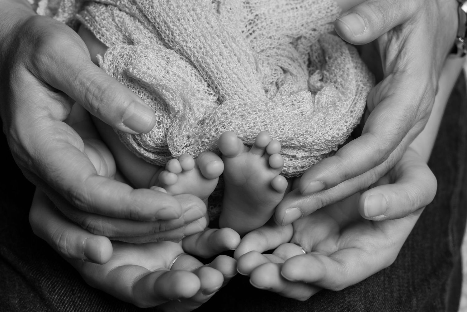 Series of black and white images showing small hands gently cradling a delicate newborn.