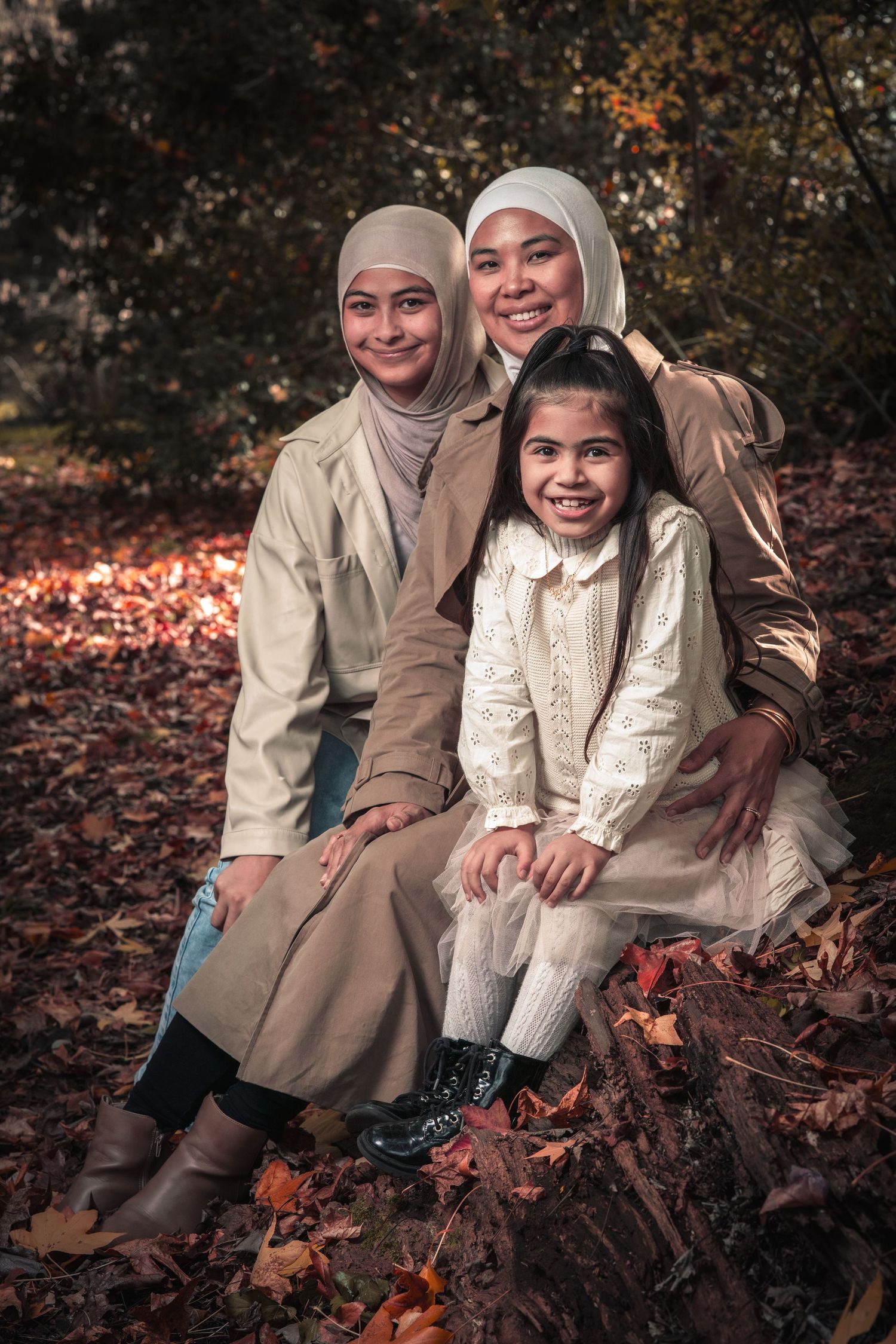 Three people posing for a portrait while sitting on autumn leaves in a forest setting.