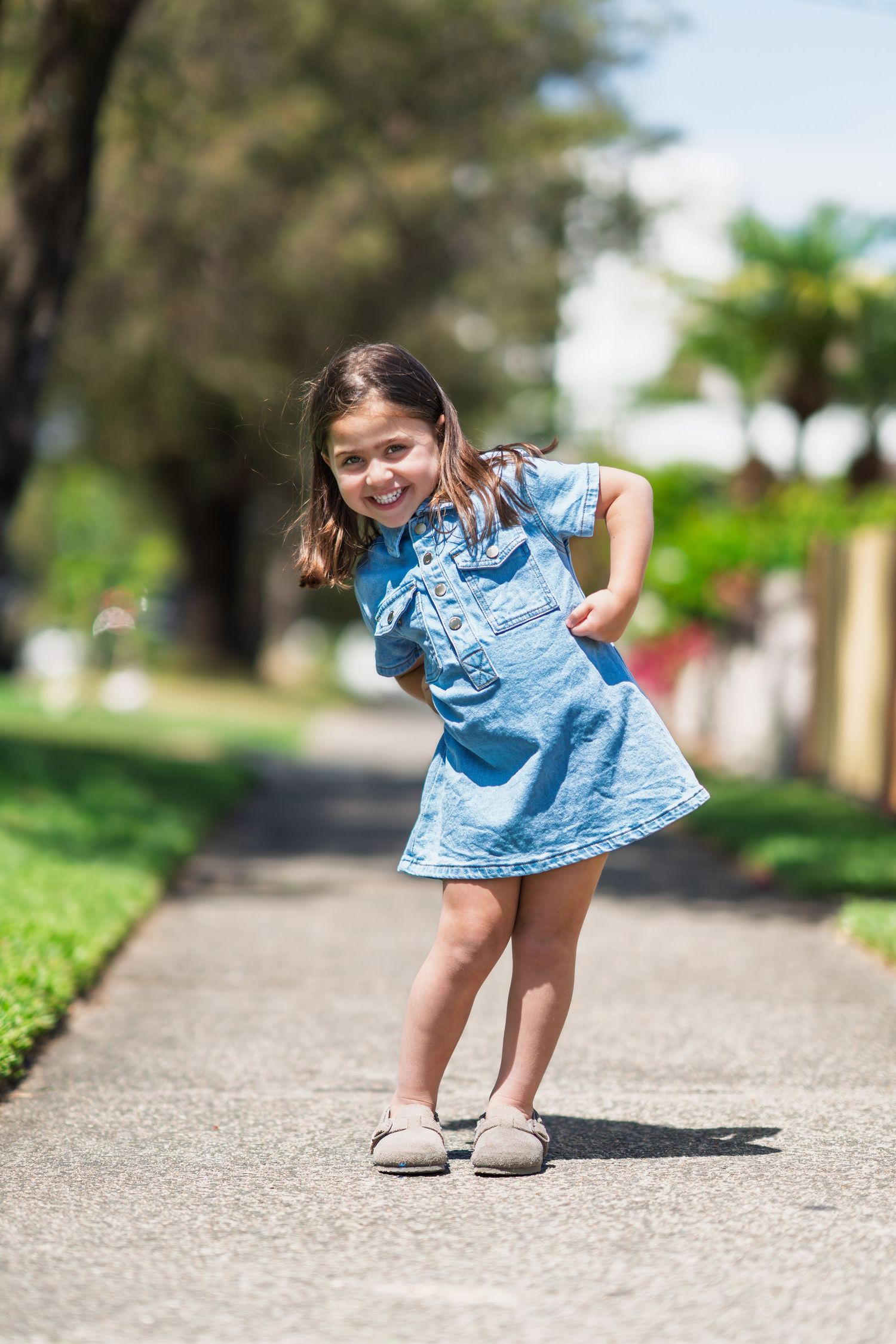 A child in a blue dress bends down to examine something on a paved path in a series of connected photos.