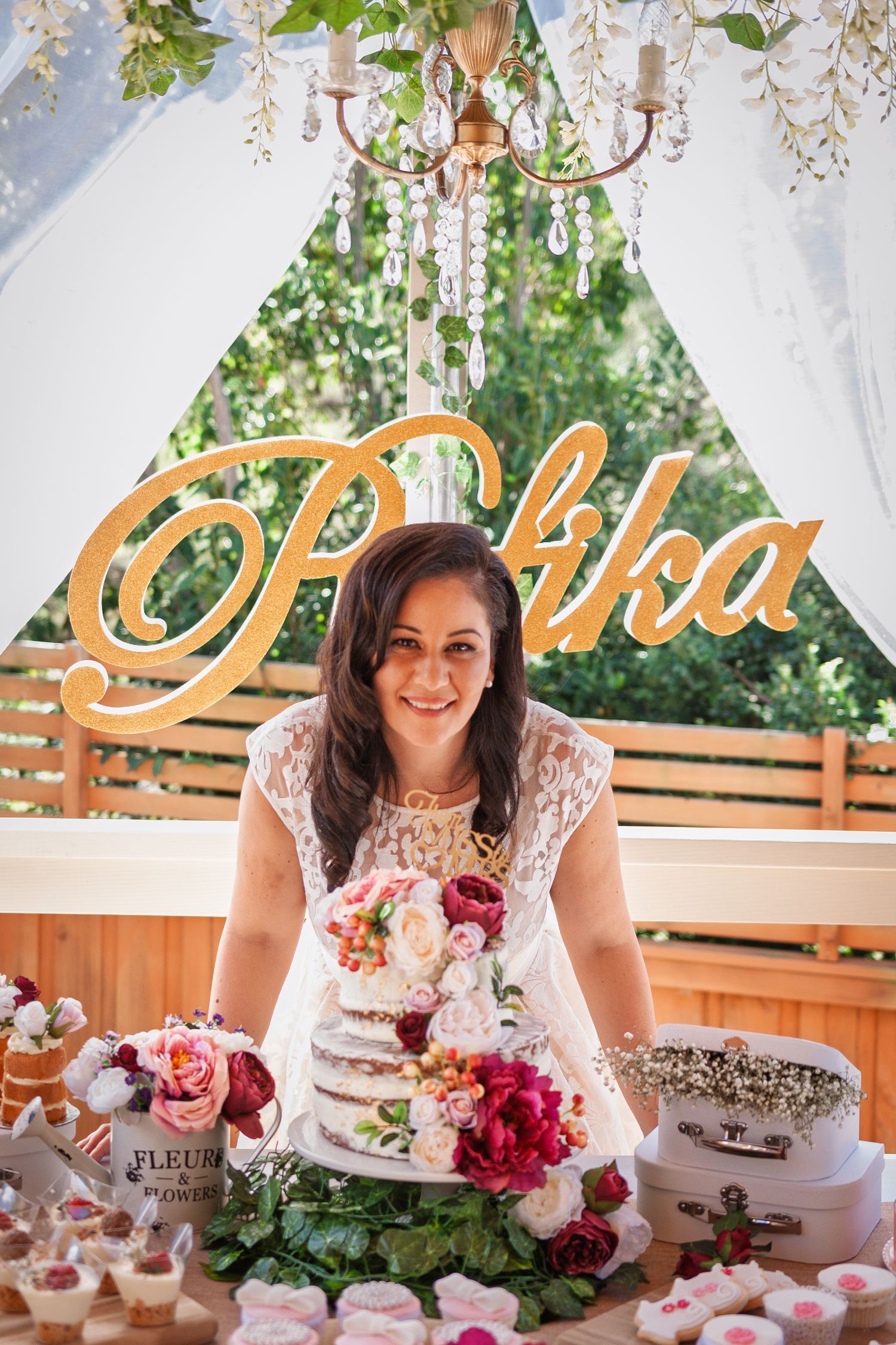 Dessert table with floral decorations and ornate signage at outdoor celebration.