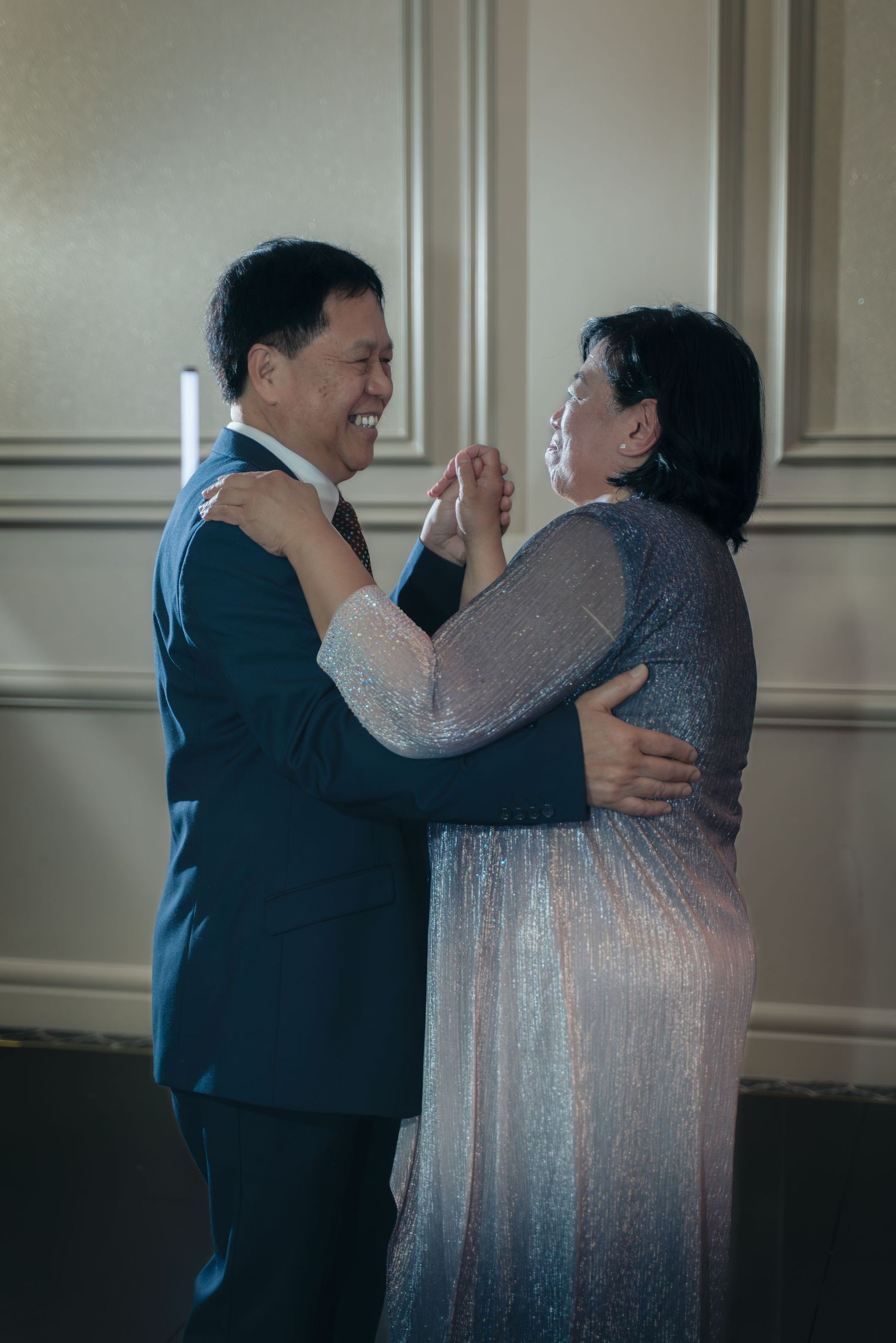 A couple in formal attire dances together in an elegant room with paneled walls.