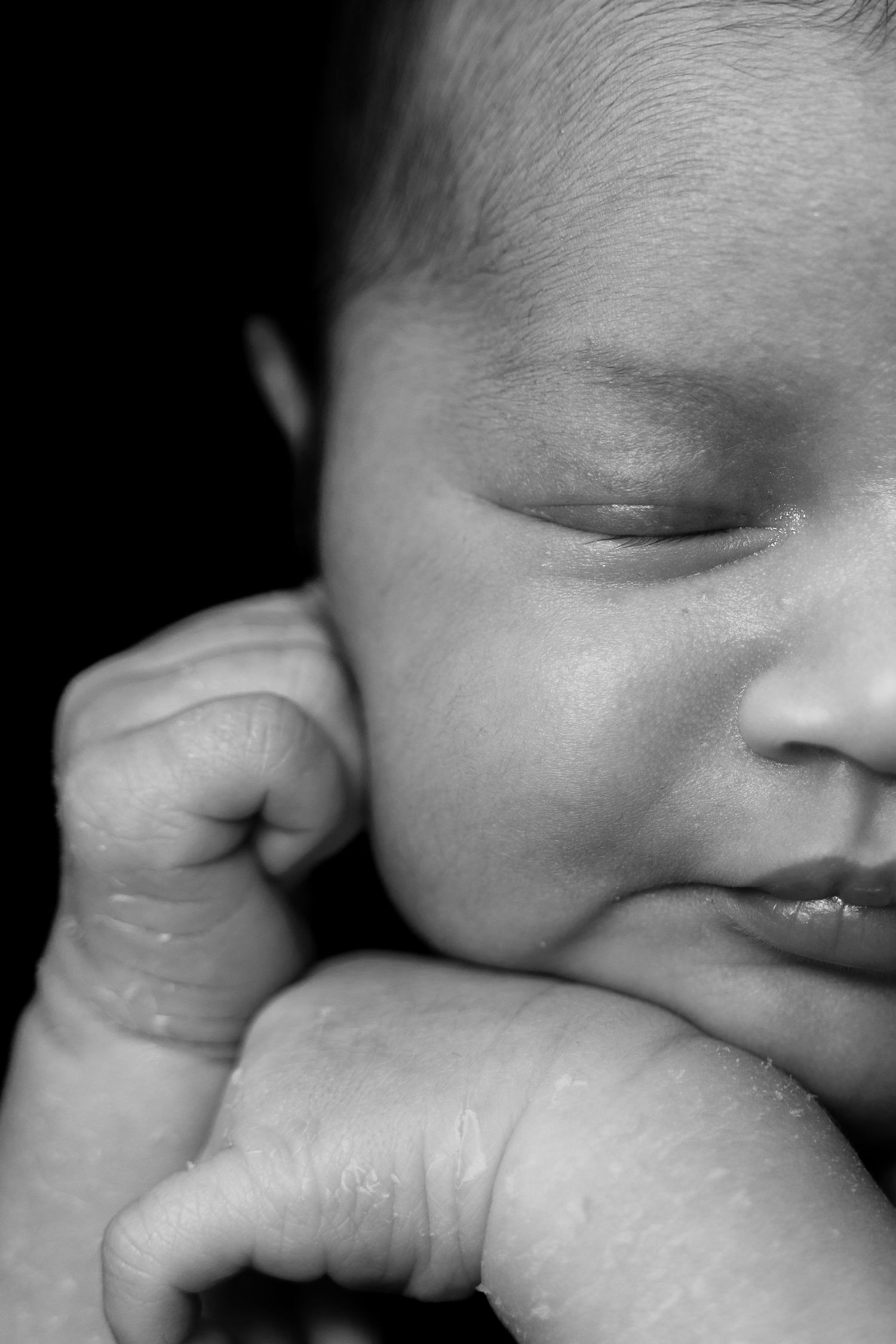 A peaceful black and white close-up of a sleeping infant's face and tiny hand.