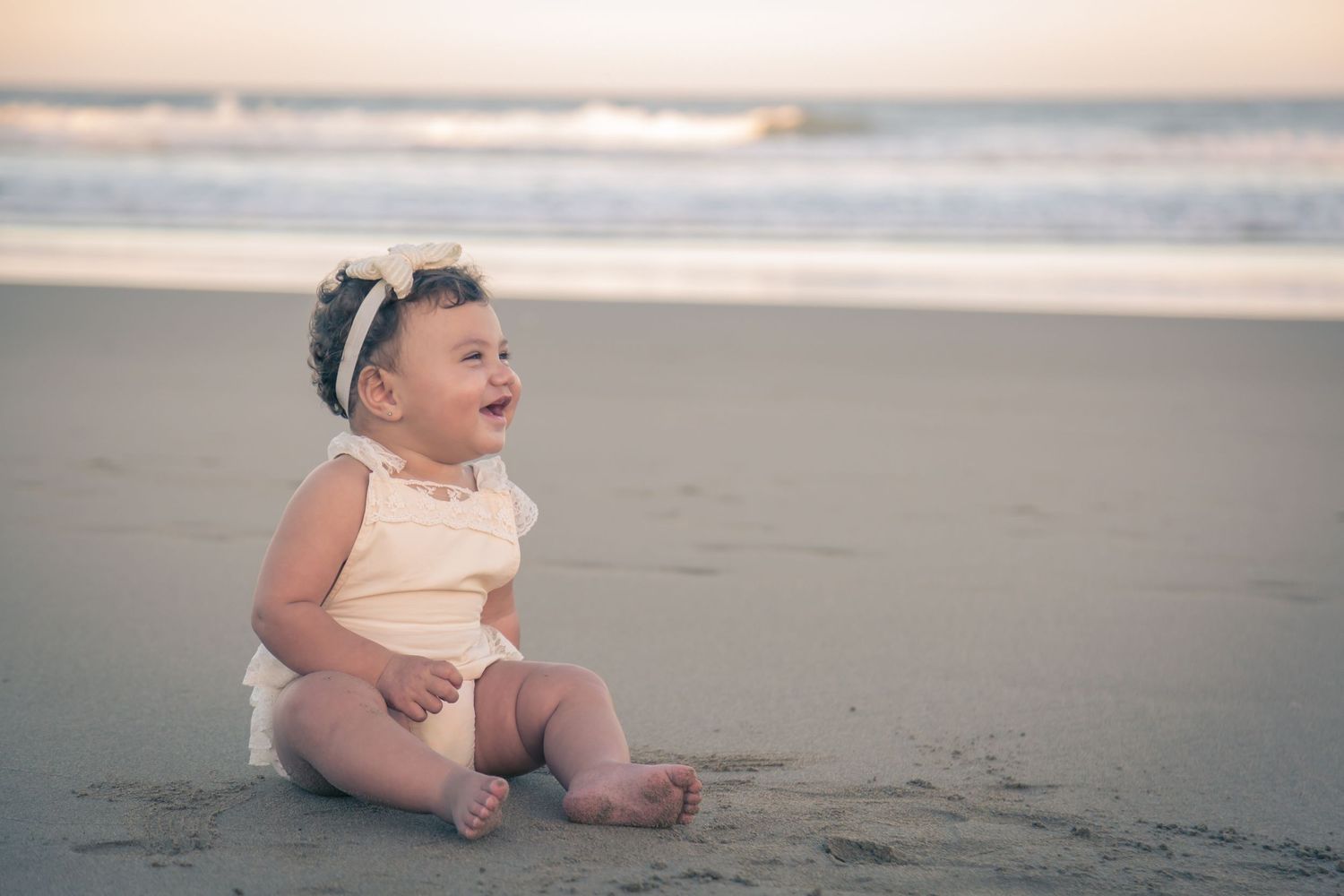 A small figure sits contentedly on the beach sand at sunset.