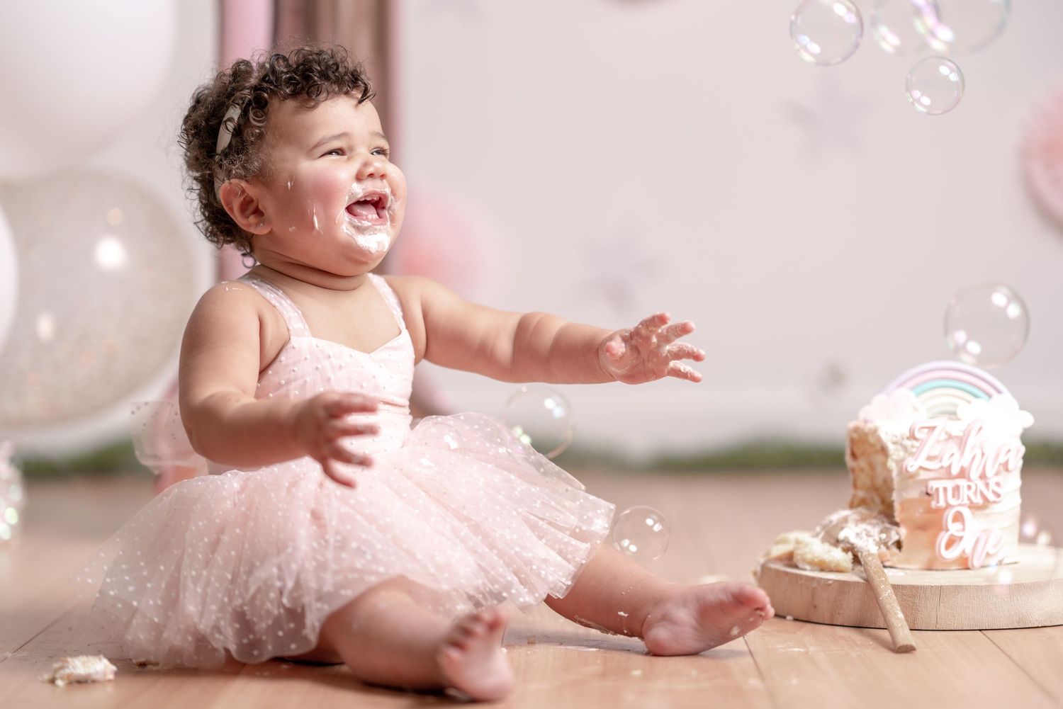 Baby in pink tutu playing with bubbles and cake during a whimsical photo session.
