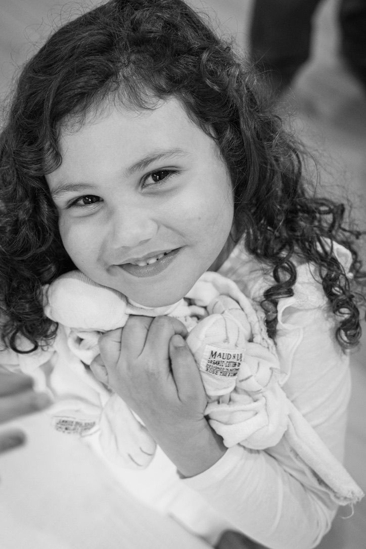 Child with curly hair holds stuffed toy while smiling in black and white portrait.