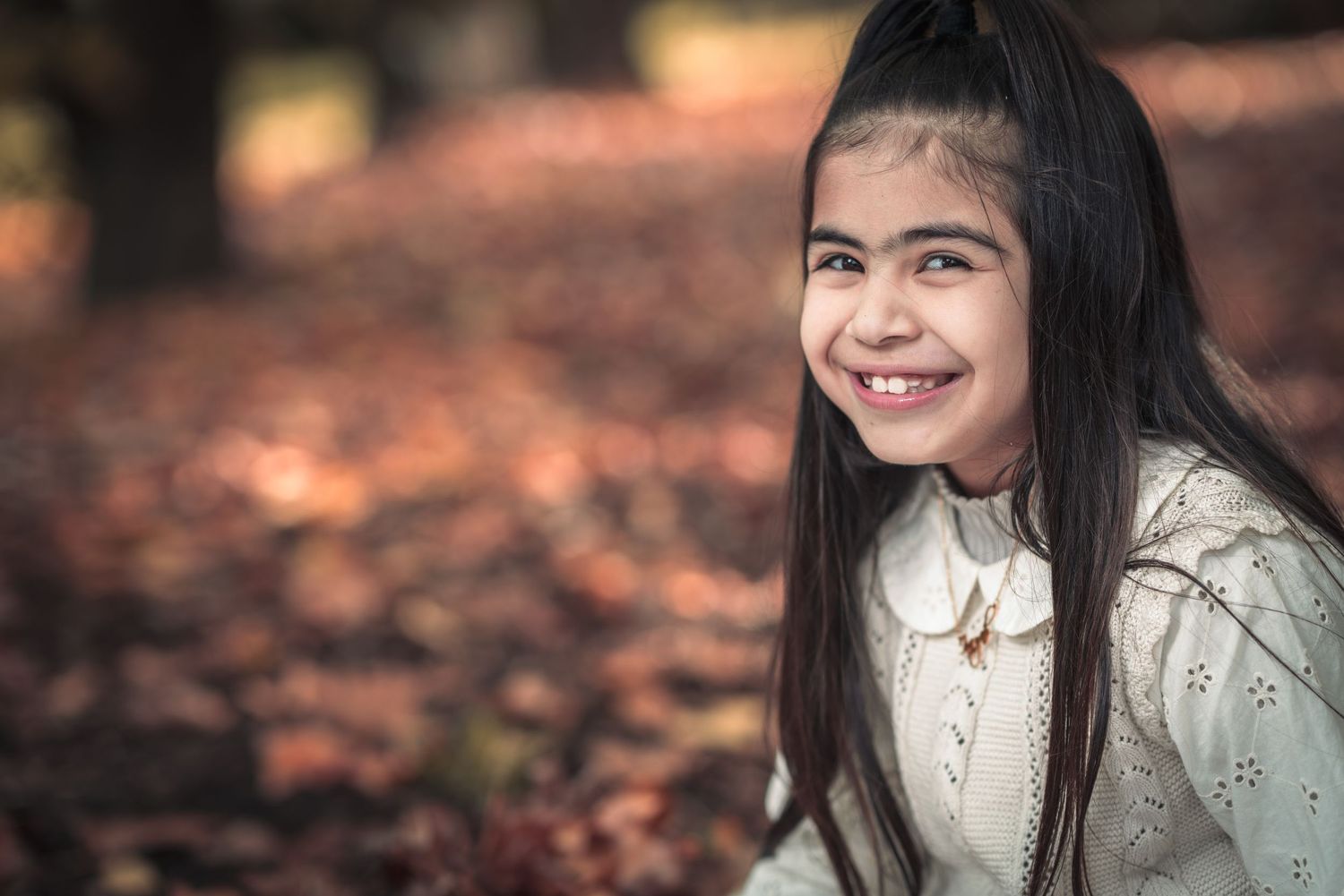 Autumn portrait against a backdrop of fallen leaves in warm lighting.