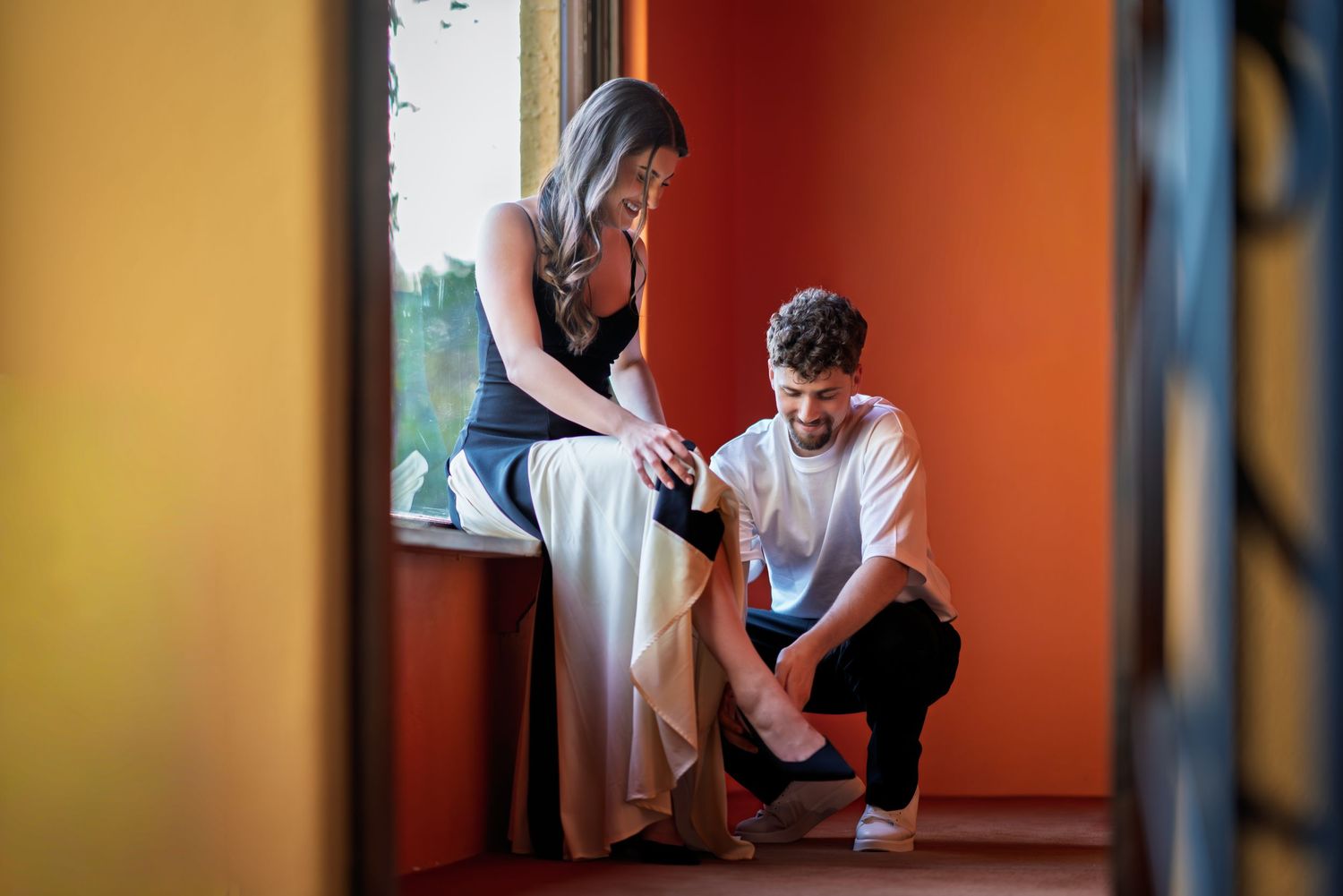 Two people share an intimate moment in a warmly lit interior space with orange walls.