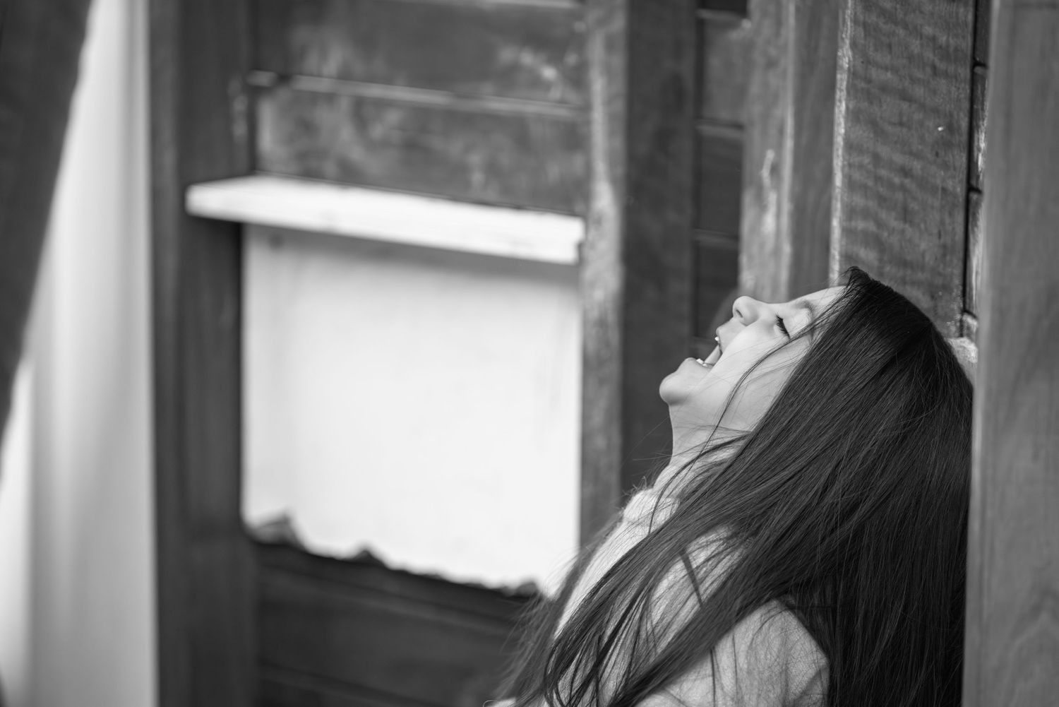 Black and white portrait of someone looking up with flowing hair near a window.