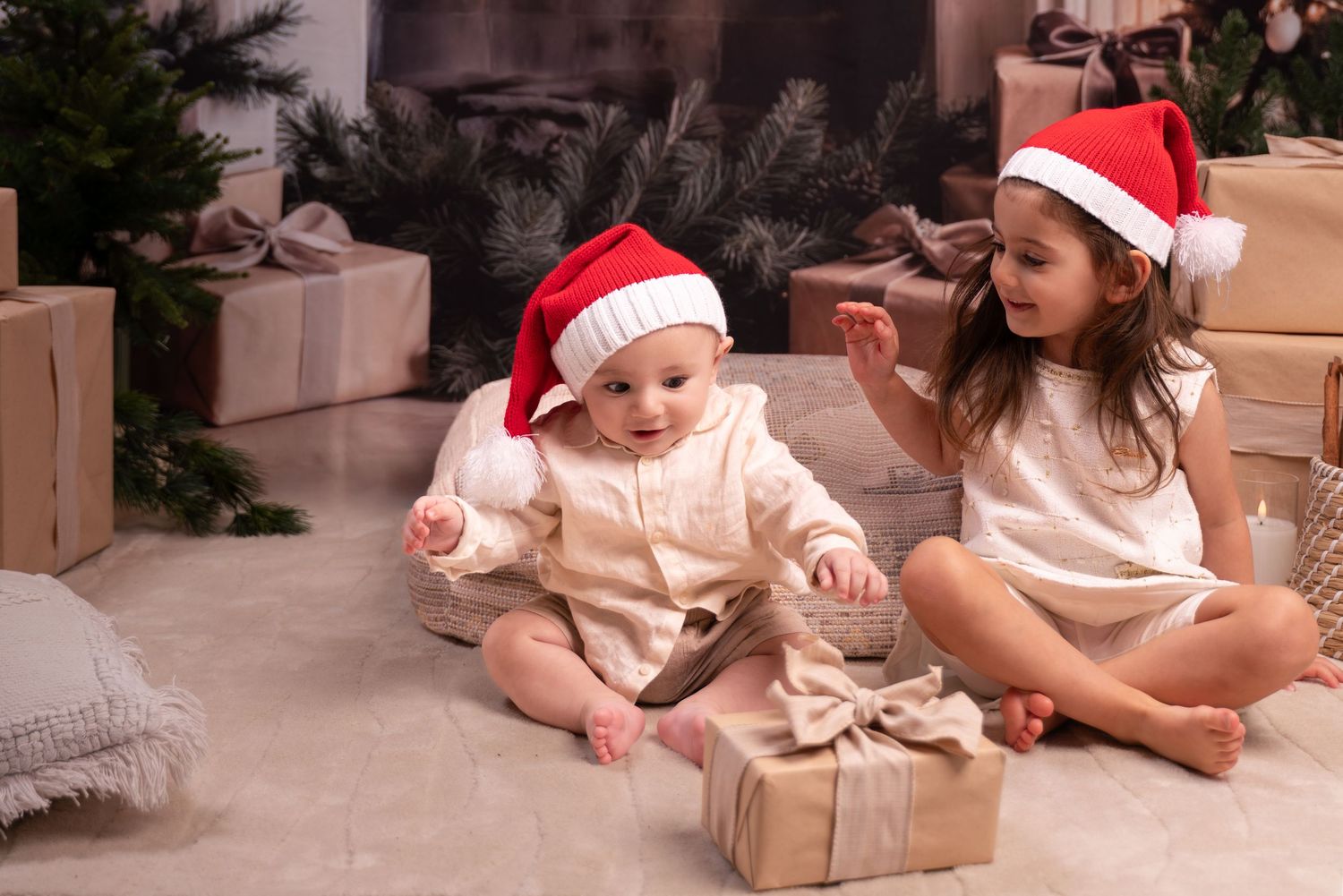 Children in festive holiday attire sit on floor opening Christmas presents near decorated tree and wrapped gifts.