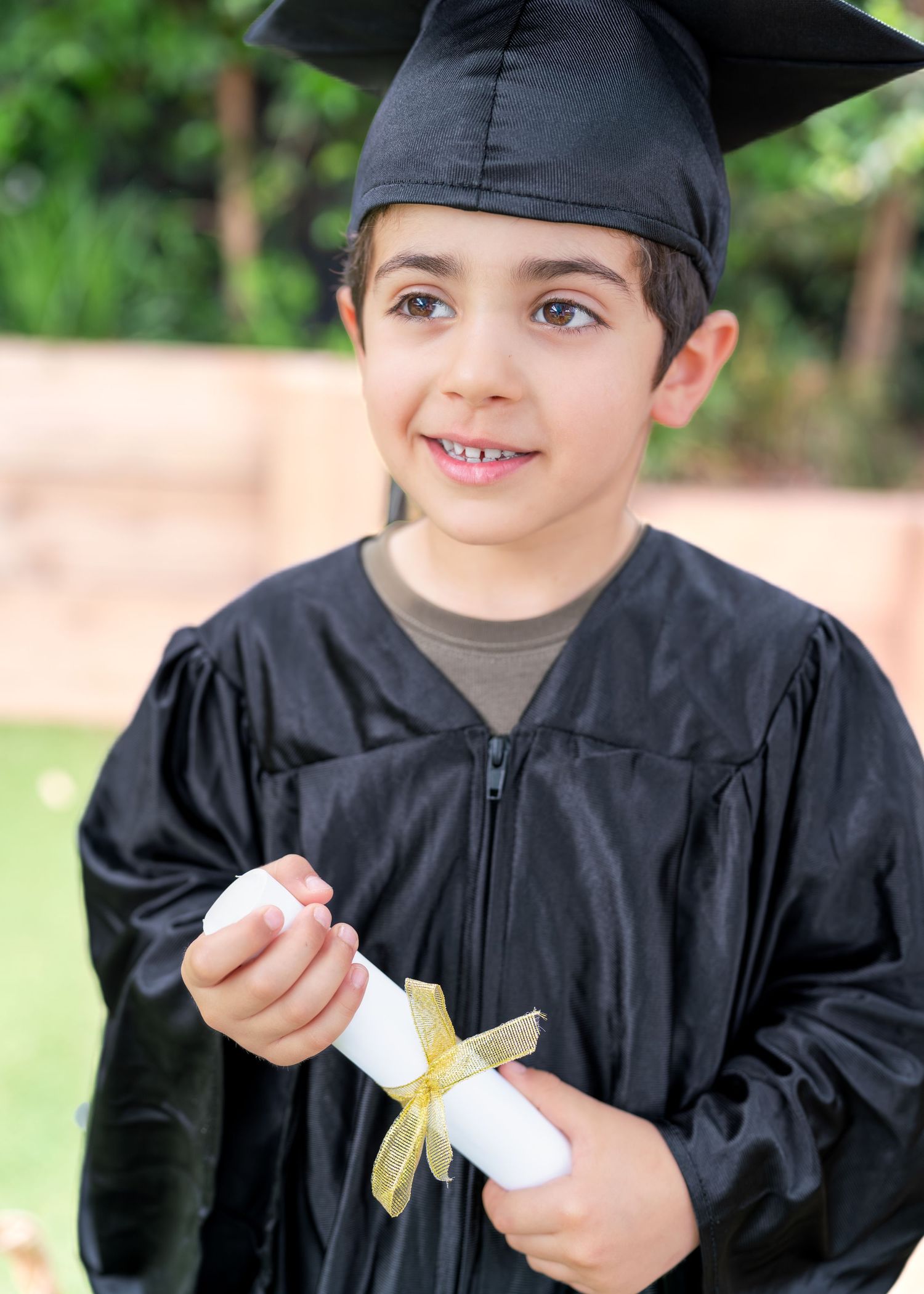Young graduate in black cap and gown unrolling diploma scroll in outdoor setting.