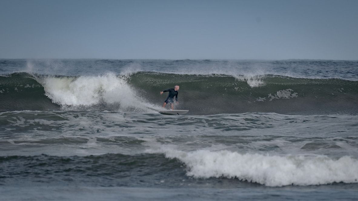 Distant surfer riding a large wave in stormy ocean conditions.
