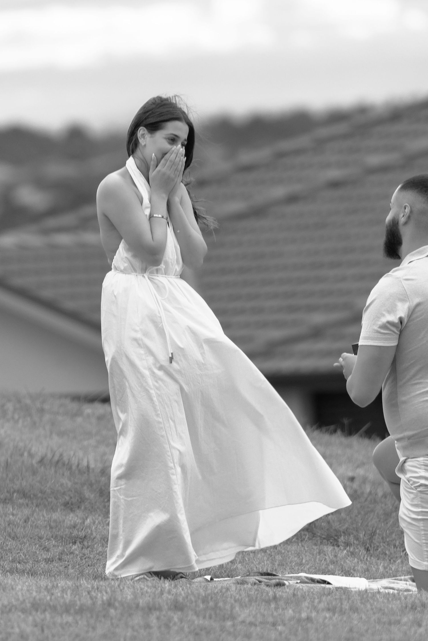 A couple in white clothing shares an emotional moment during an outdoor photoshoot in a grassy field.