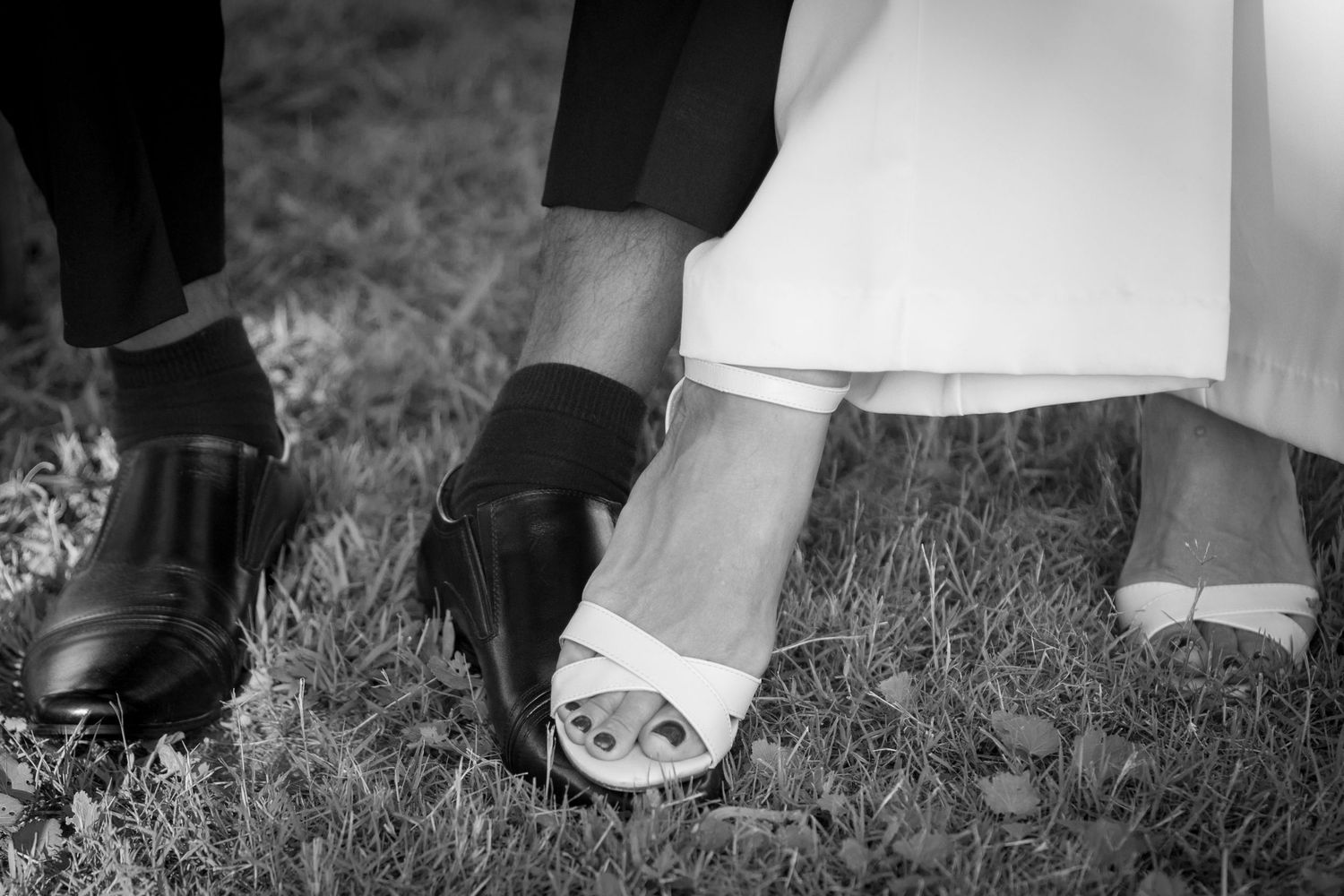 Black and white detail shot of formal shoes and dress hems on grass.