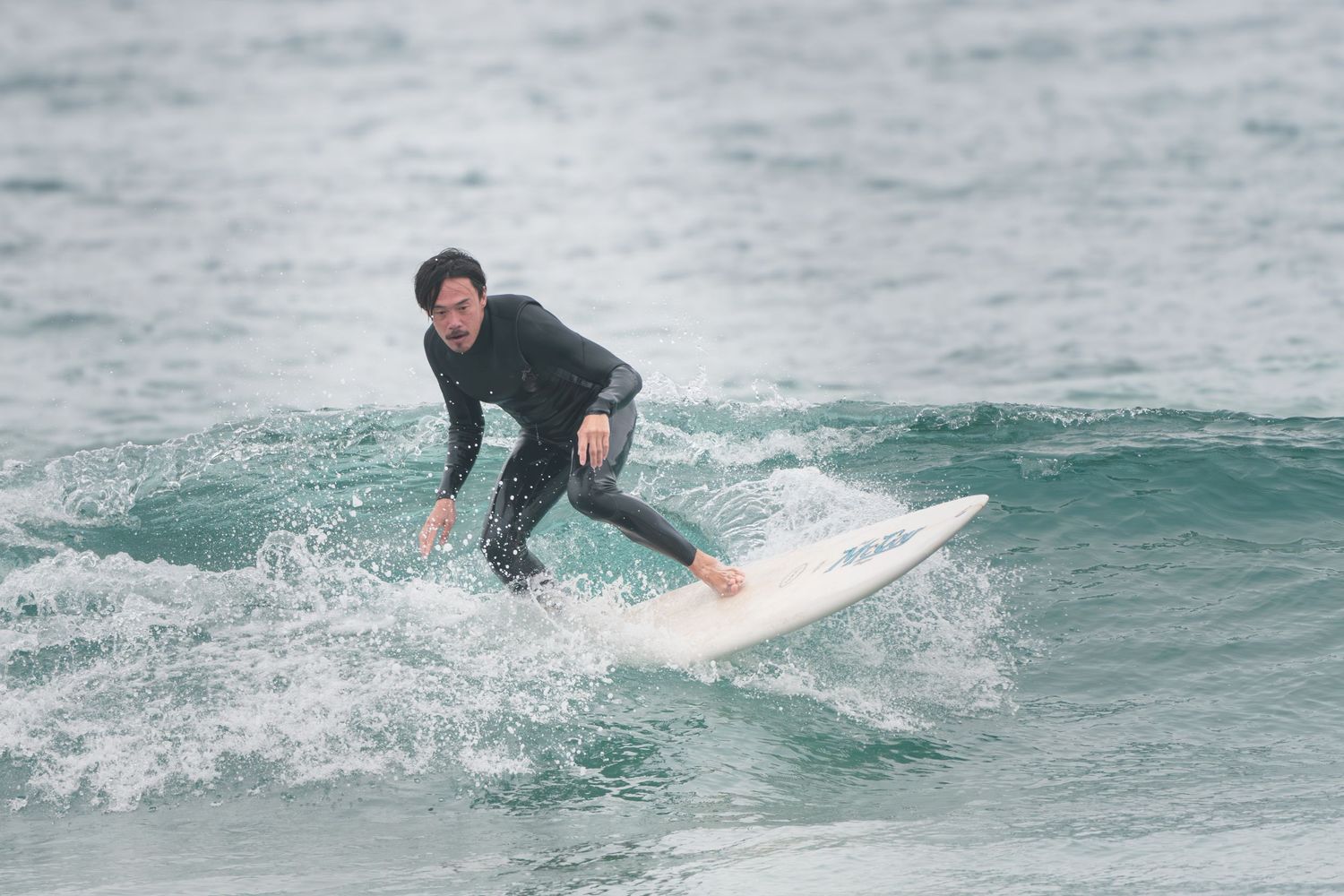 A surfer rides a wave in a black wetsuit during a cloudy day at sea.