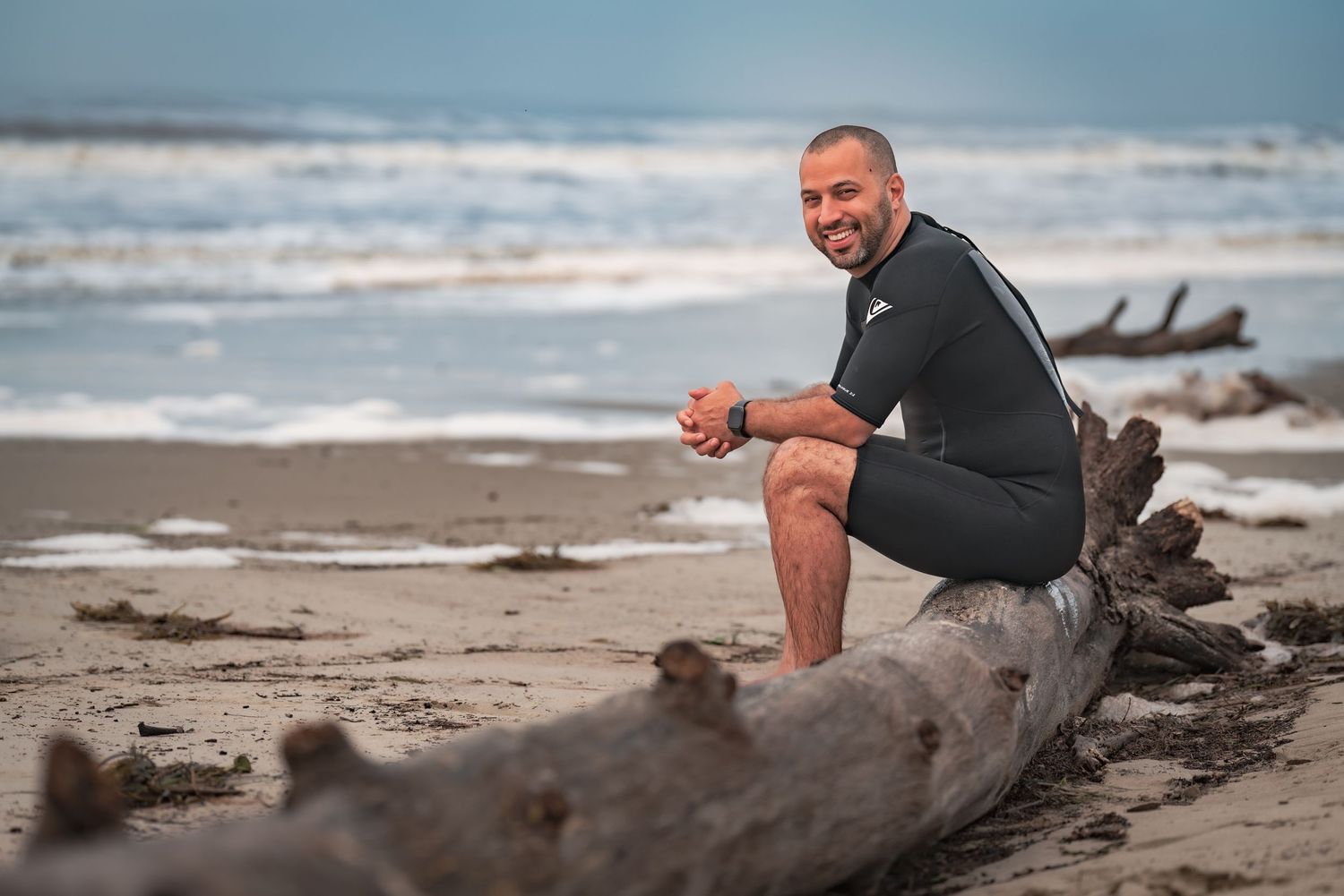 Person relaxing on driftwood at a beach during sunset.