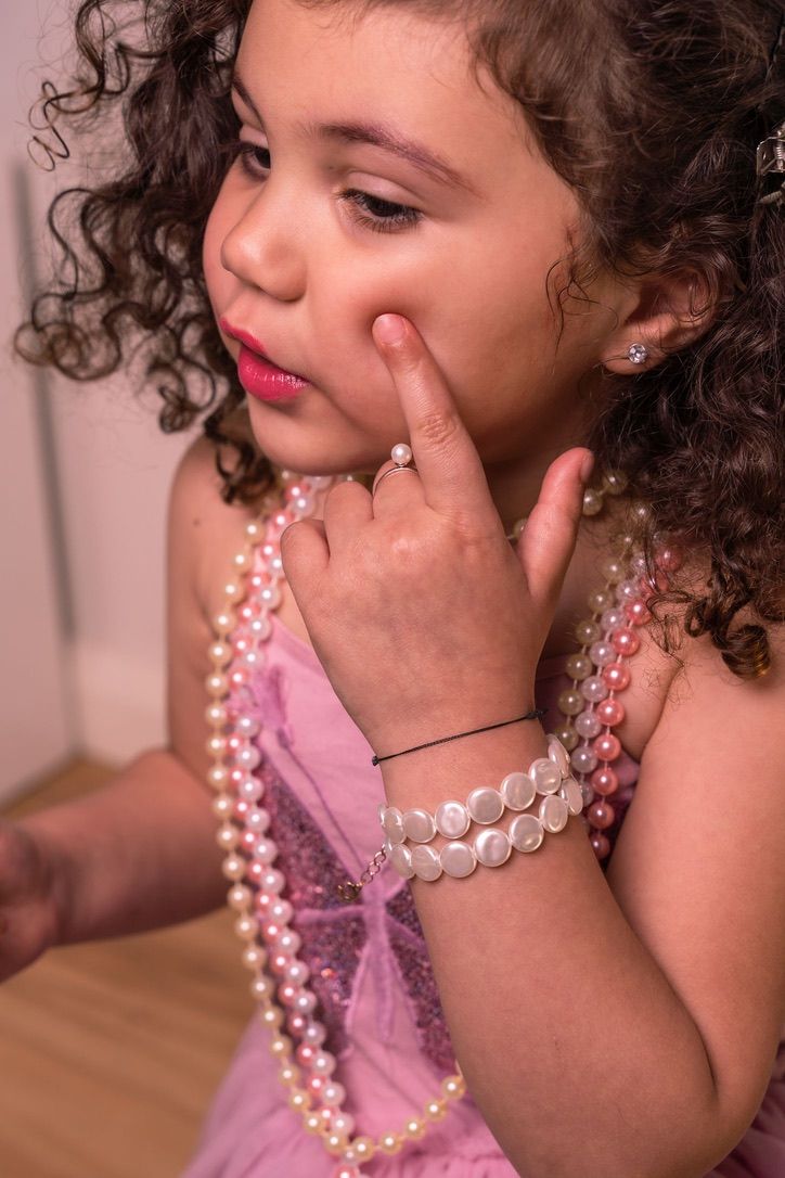 A thoughtful pose showing curly hair, pearls and a pink dress with delicate details.