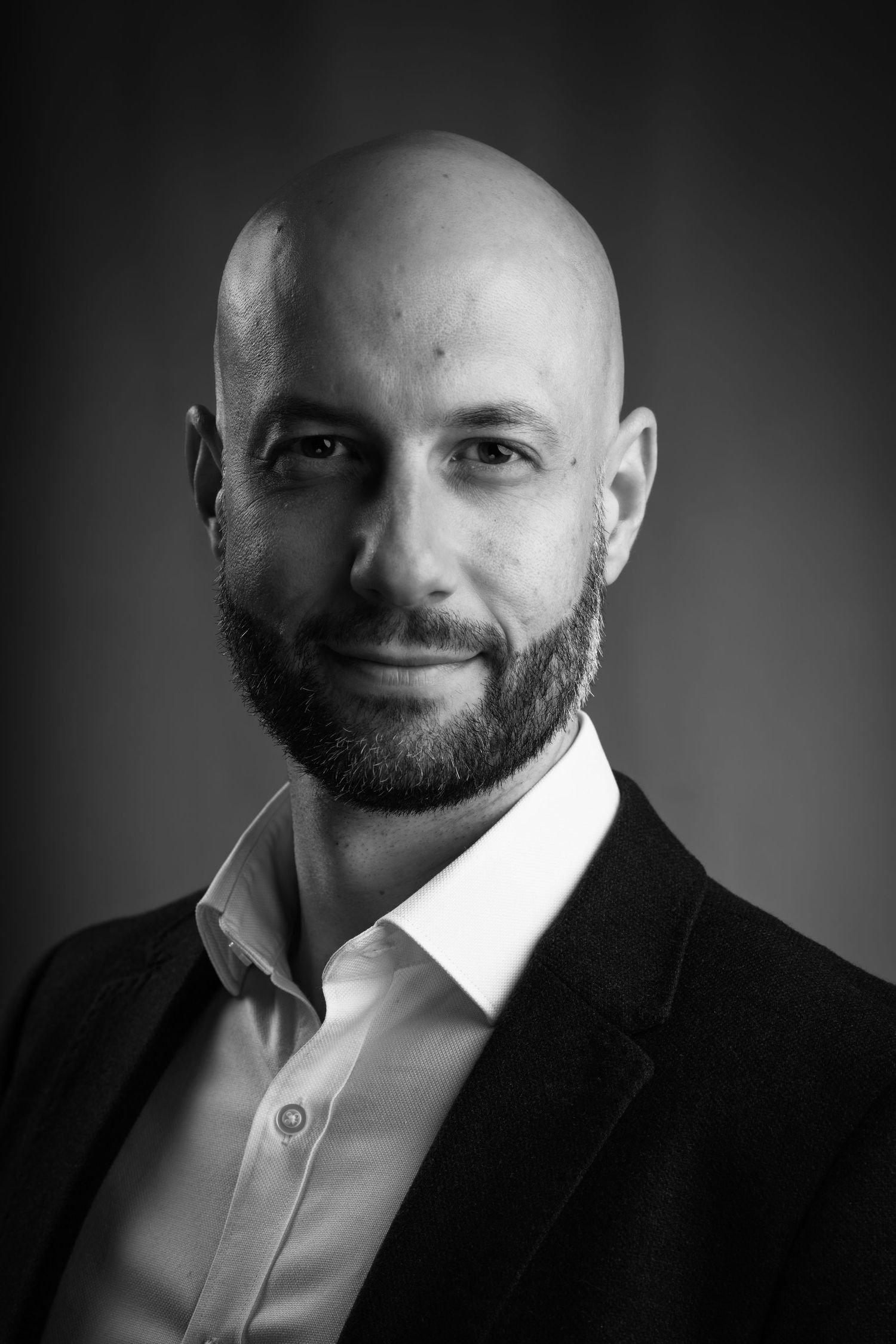 Professional black and white headshot of a bald executive with beard wearing blazer and white dress shirt.