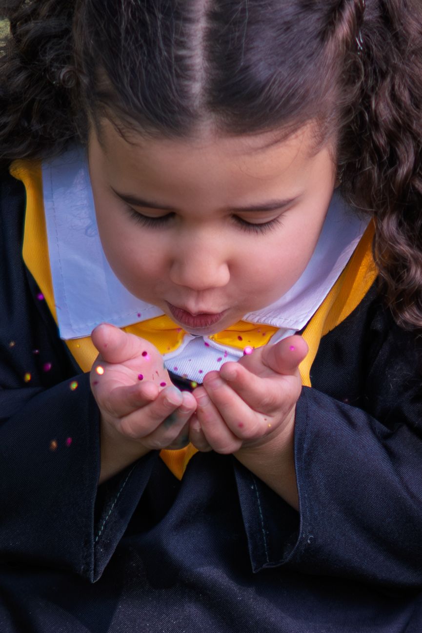 Child in yellow uniform gives a gentle kiss to a pink toy held close to their face.