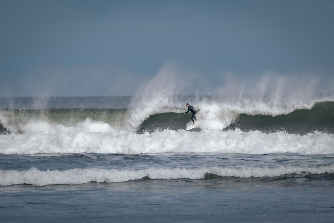 Silhouetted surfer catching air off a large breaking wave in misty conditions.