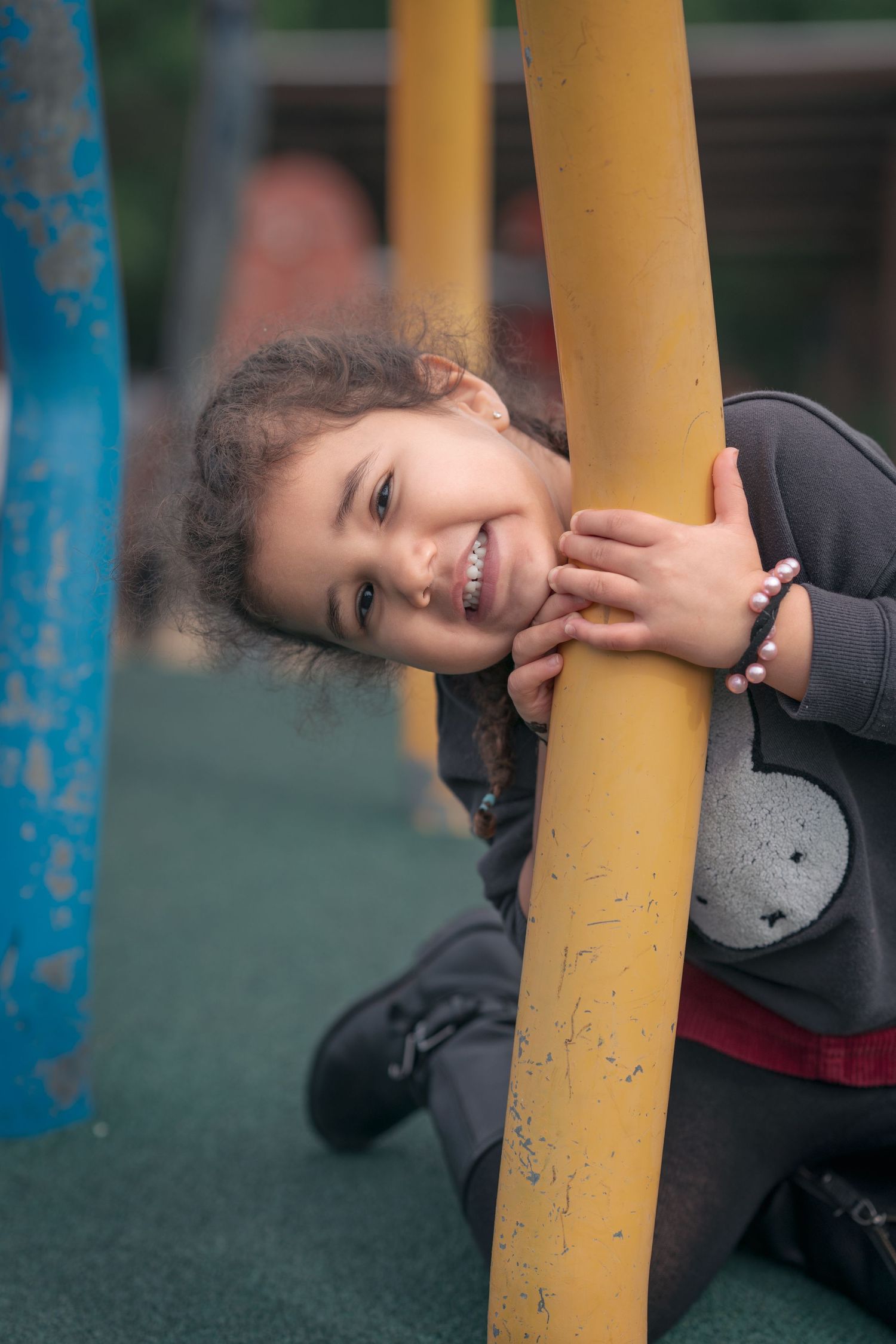 A child playfully hugs a yellow pole on a playground.