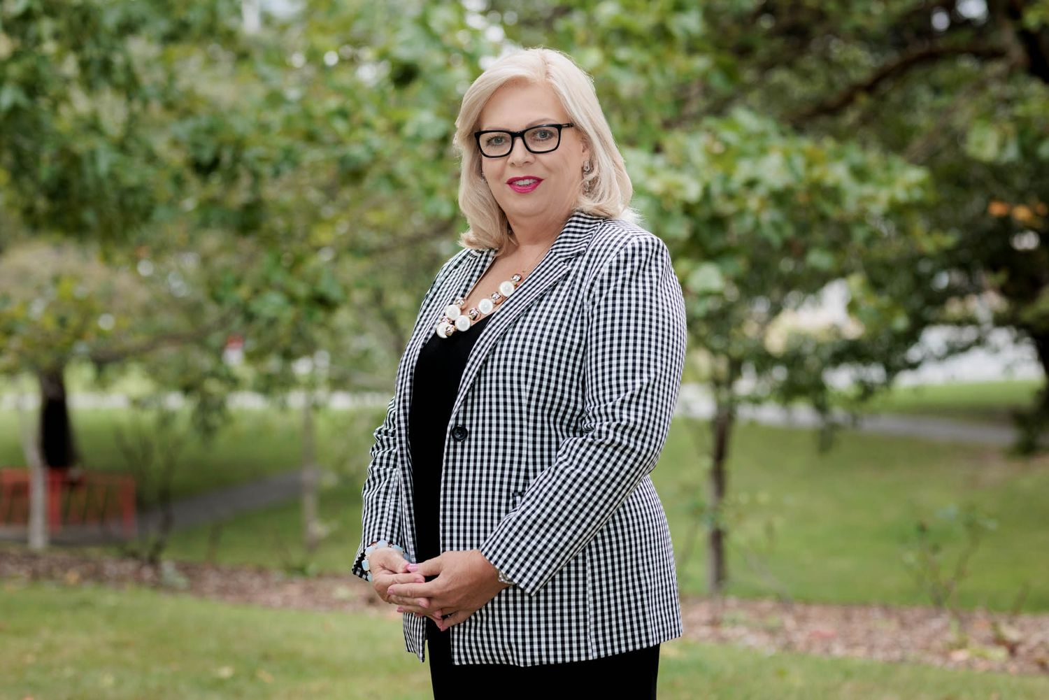 Outdoor professional portrait of a real estate agent in business attire among green foliage.