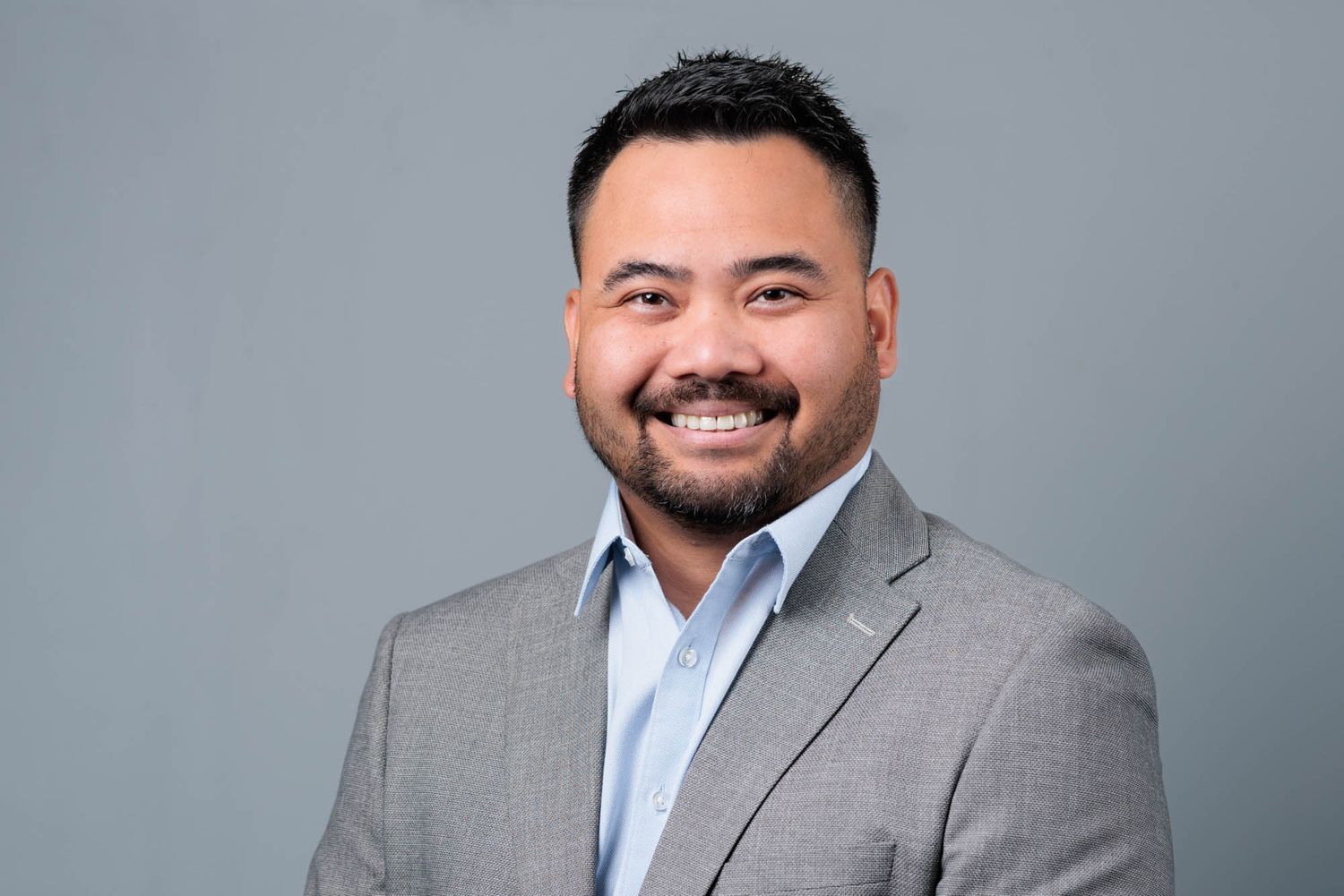 Professional headshot against grey background wearing business attire.