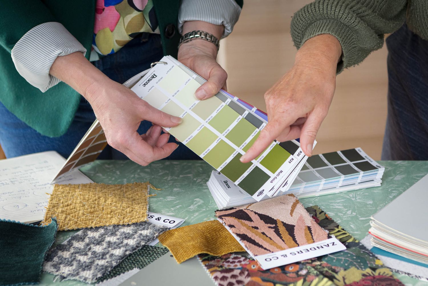 Close-up of hands examining color swatches and material samples on a wooden surface.