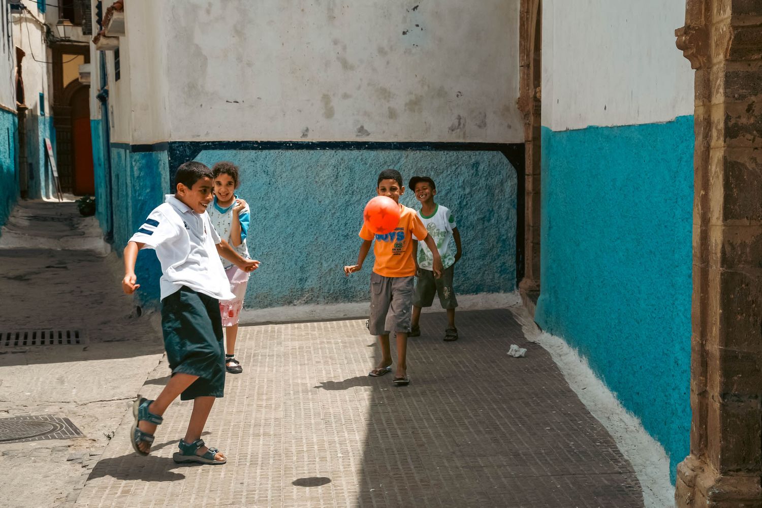 Urban alley in the Rabat Medina with blue and white walls where children play in the sunlight.