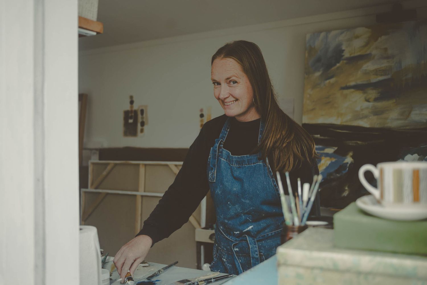 Artist in denim overalls working in a bright studio space.