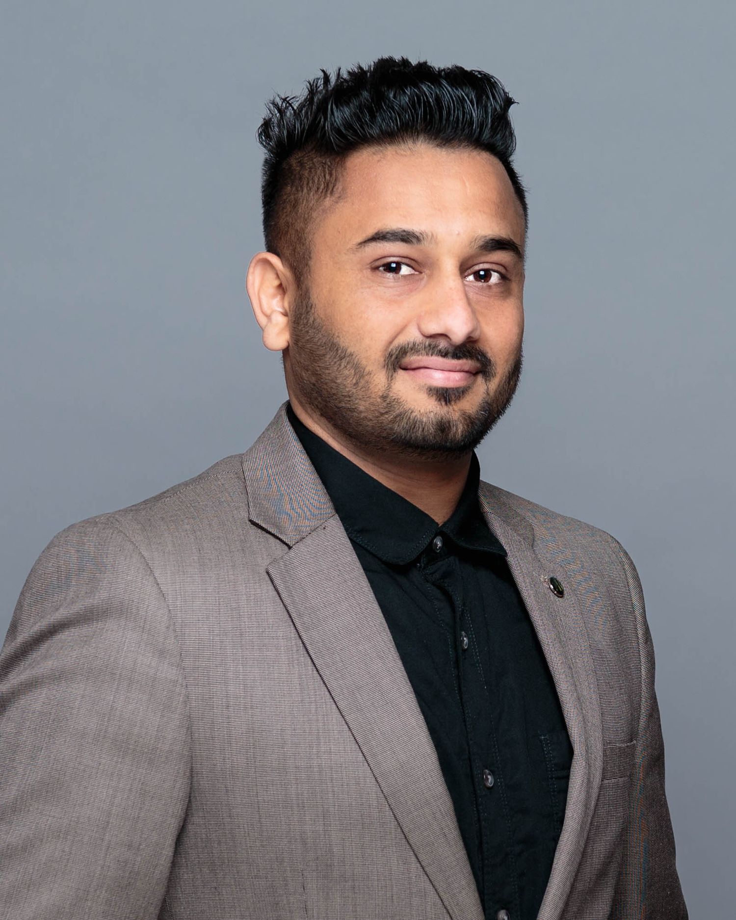 Business portrait of a person wearing a gray suit jacket and black polo against a gray background.