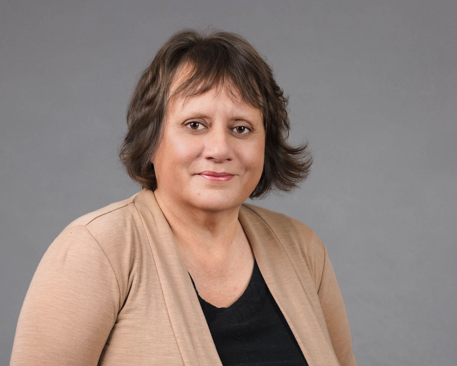Professional headshot of a person in business attire against a gray studio background.