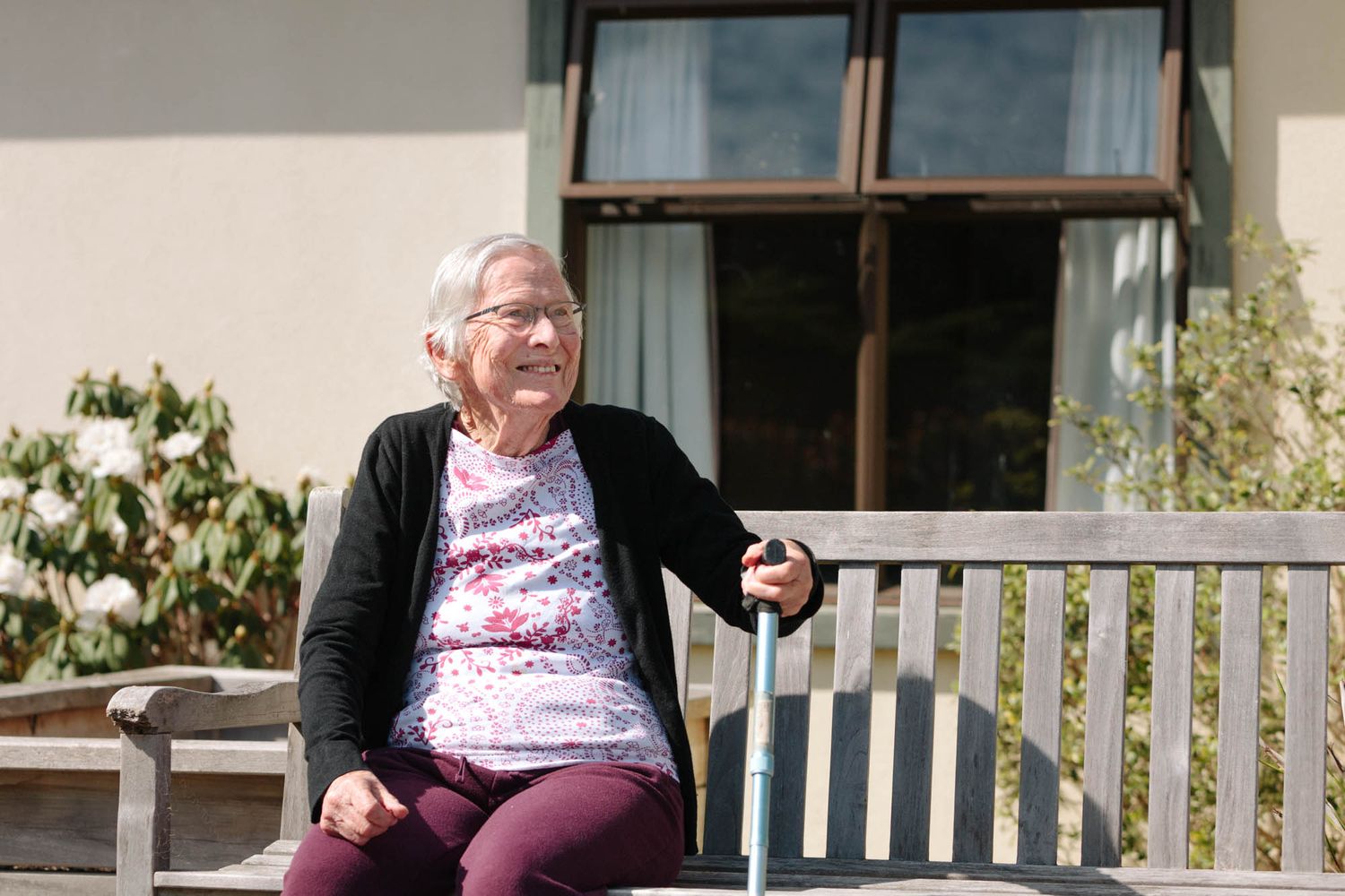 Sunny outdoor seating area with white benches where an elderly lady is relaxing.
