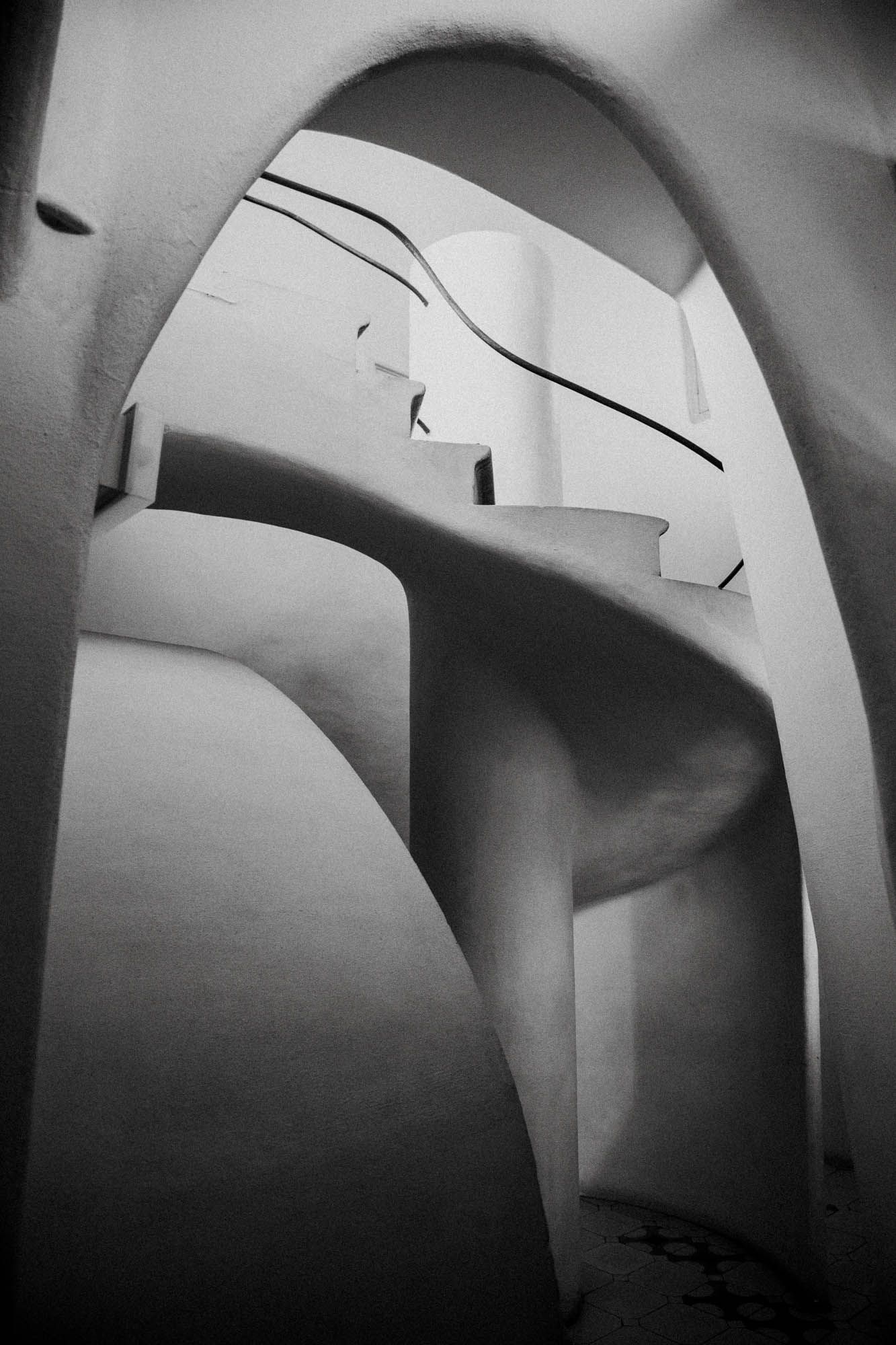 Series of curved architectural arches by Gaudi creating dramatic shadows in black and white.
