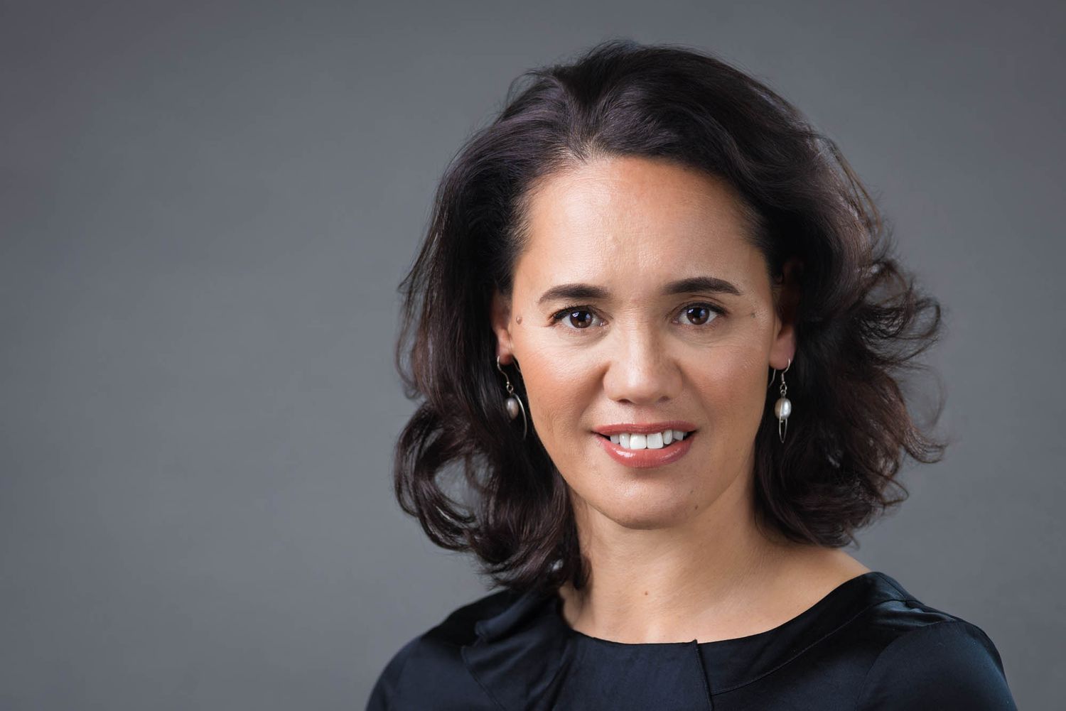 Professional headshot of Merewaakana Kingi against a gray studio background.