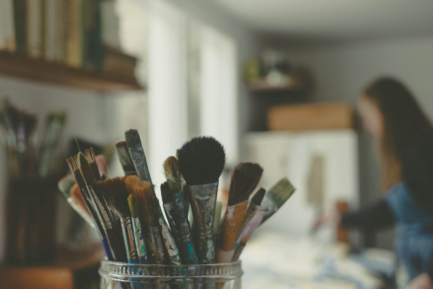Collection of art brushes standing in a glass jar with soft focus background.