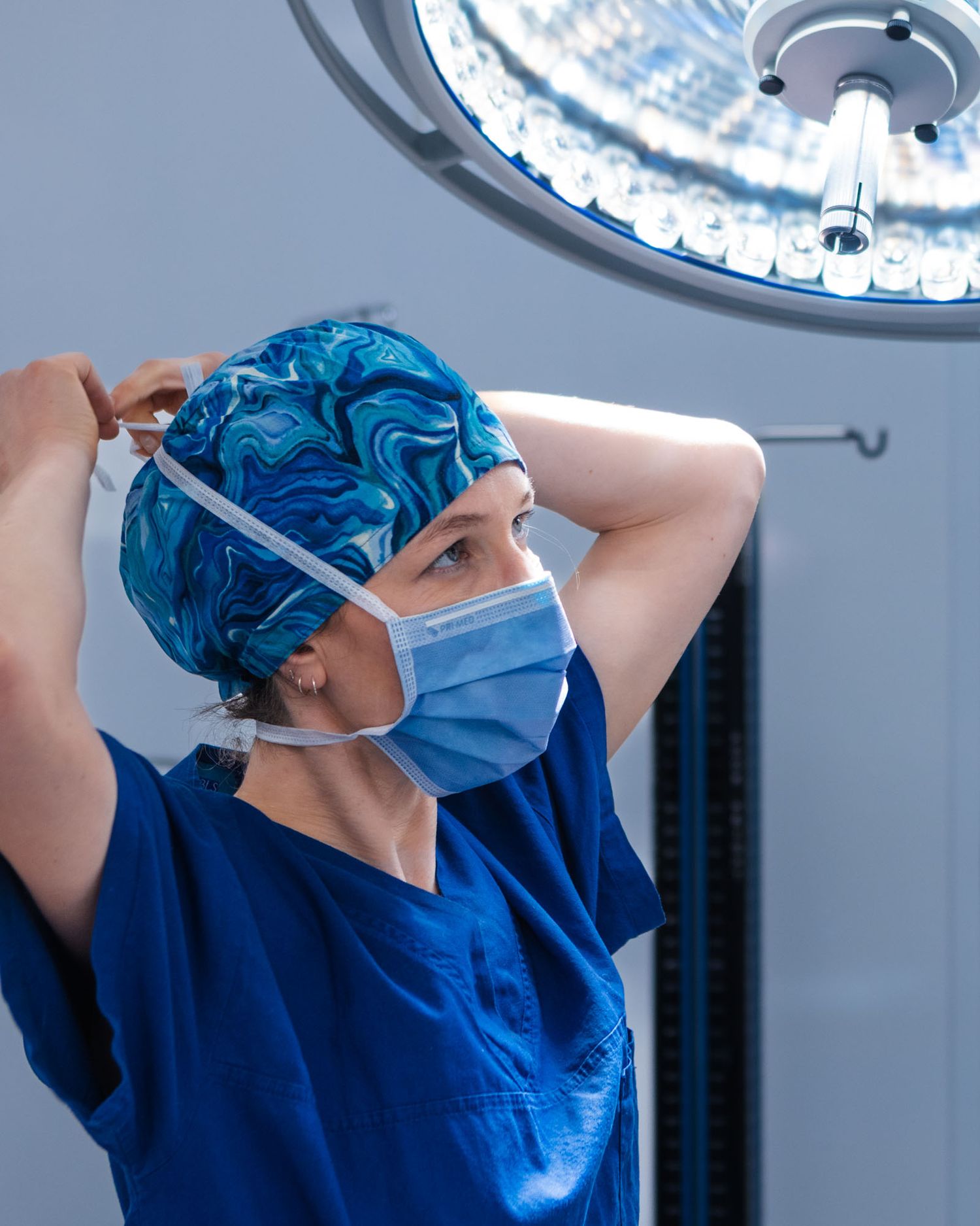 Medical professional in blue scrubs and surgical cap preparing for procedure.