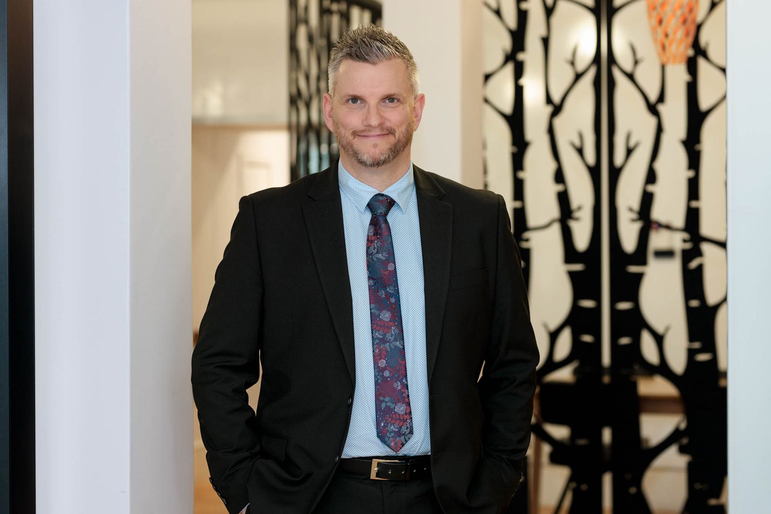 Professional staff member in business attire standing in an elegant hallway with decorative wall panels.
