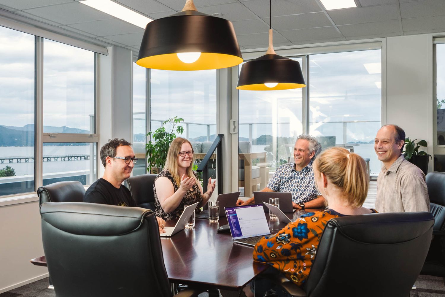 Arlo conference room with large windows, pendant lights and people gathered for a meeting.