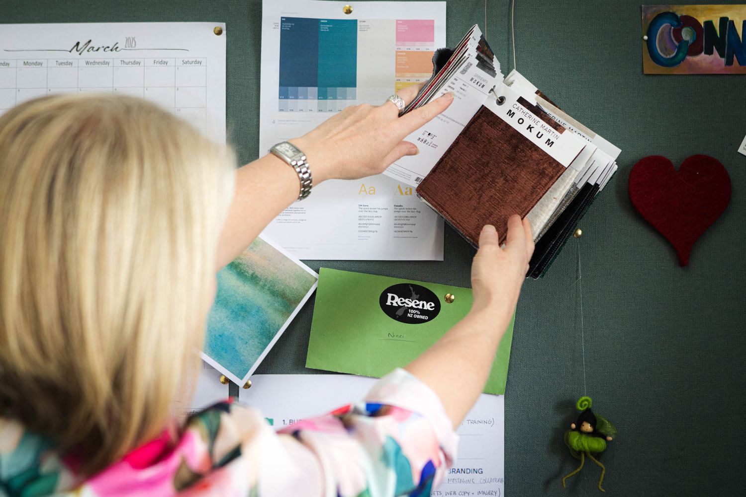 Hands holding and arranging papers against a green wall with photos and decorations.