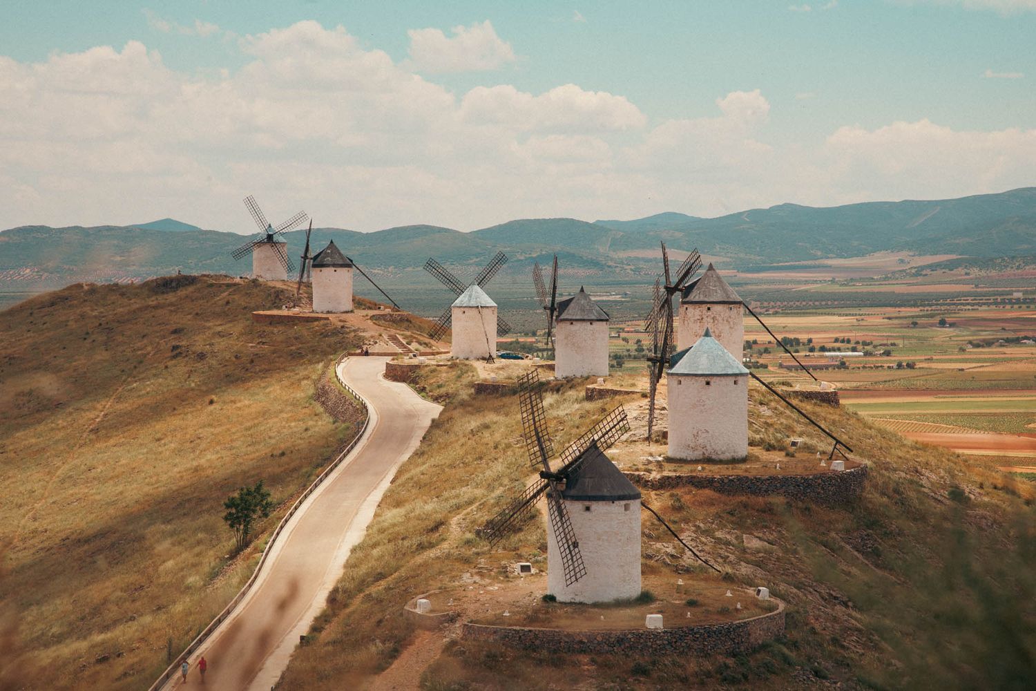 Row of traditional windmills on a hilltop against a blue sky with white clouds near Consuegra.