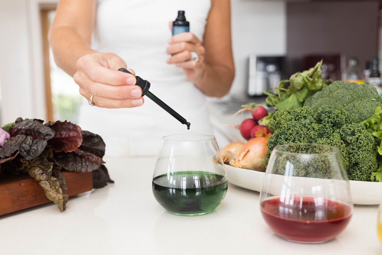 Hands preparing healthy ingredients and adding drops from dropper bottle in modern kitchen.